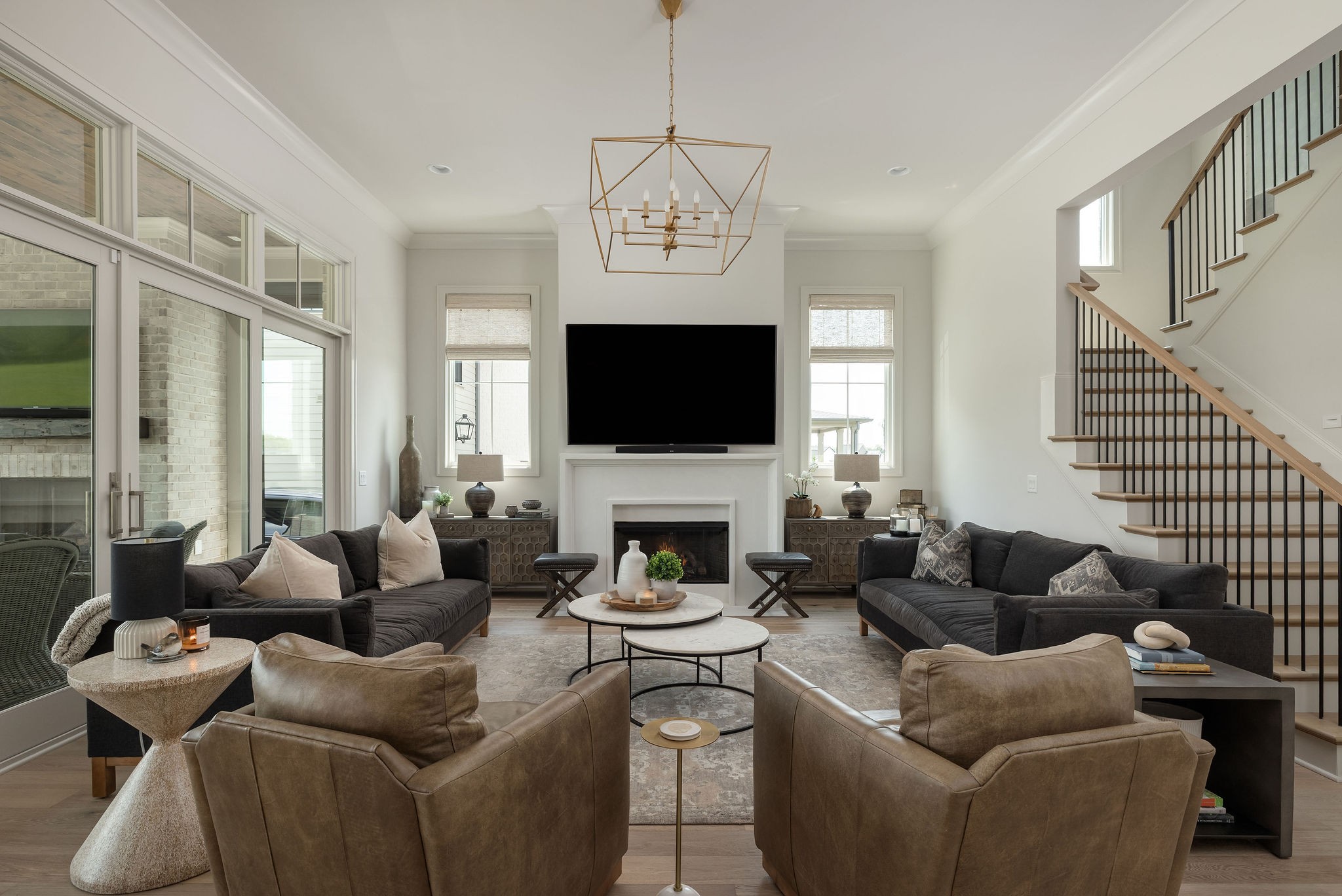 Furnished living room with fireplace, large television, dark sofas, and staircase with black railings.