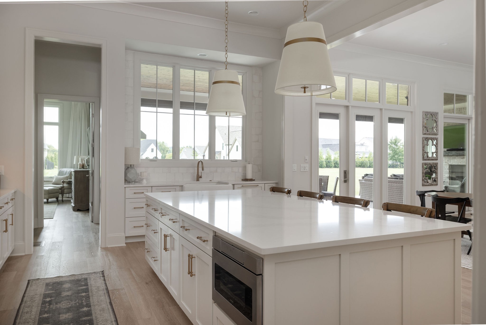 Bright white kitchen with a large island, brass hardware, and windows overlooking the yard.