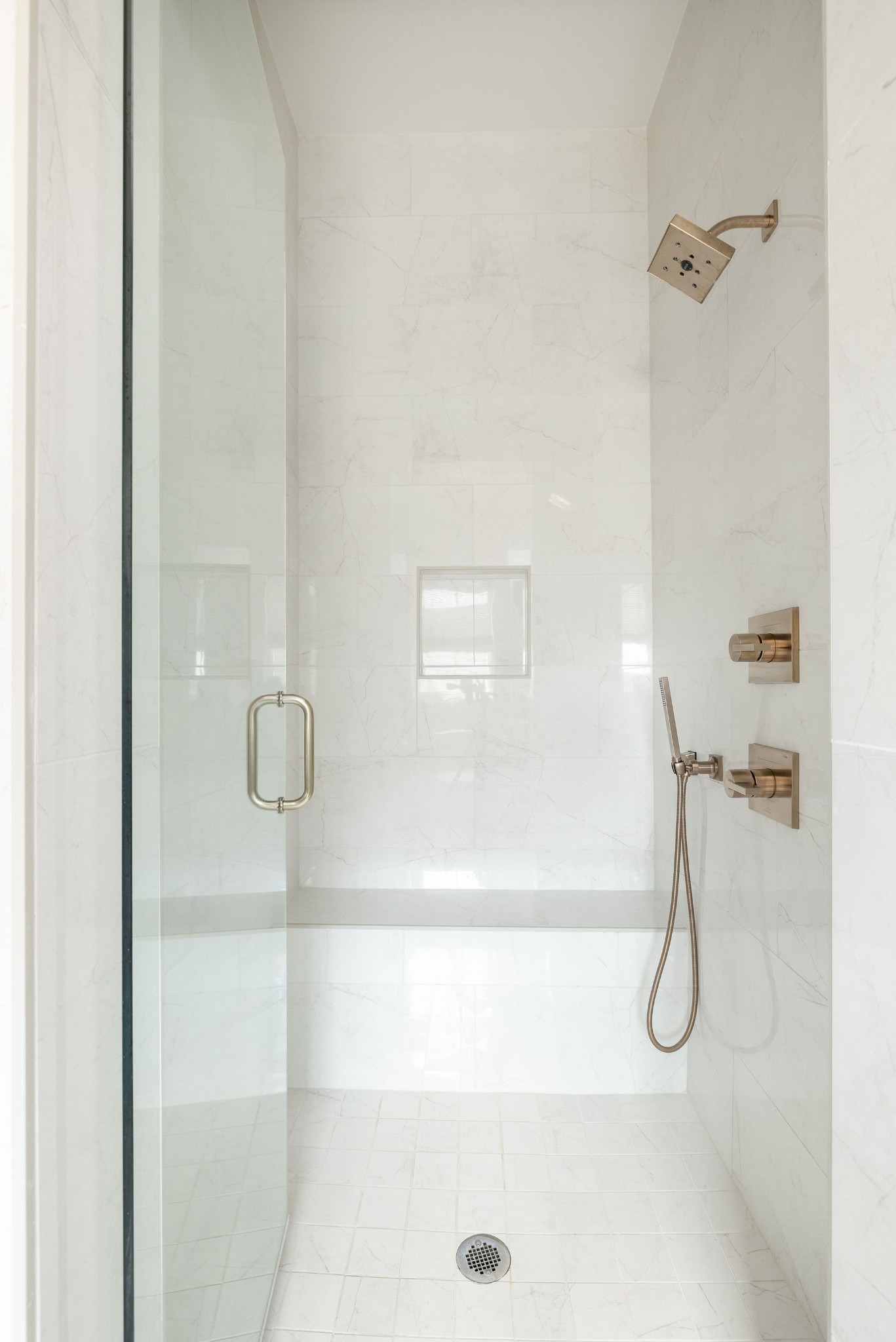 Walk-in shower with white veined tile, glass door, and brushed bronze fixtures.