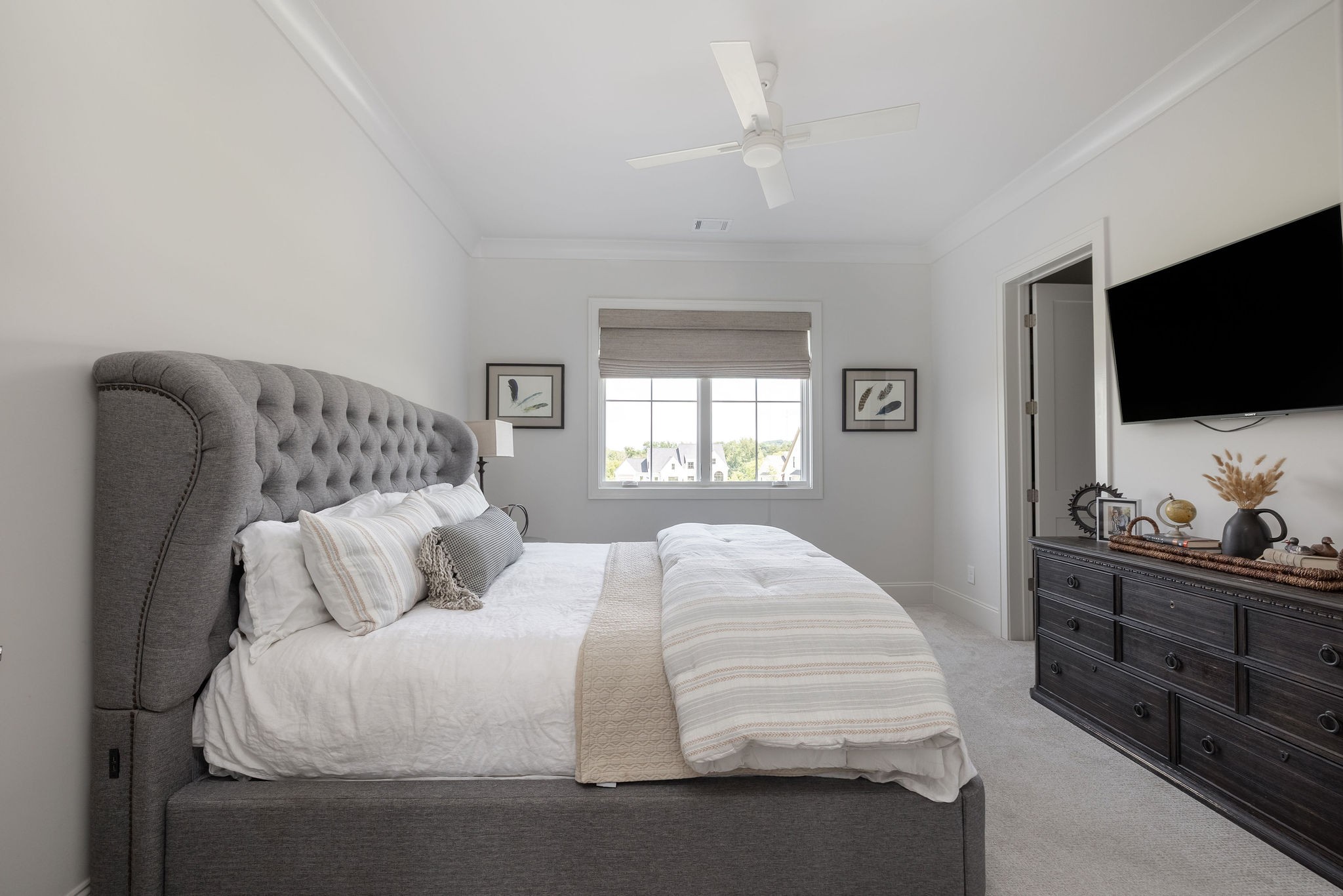 Bedroom with a gray tufted bed, dark dresser, wall-mounted television, and window.