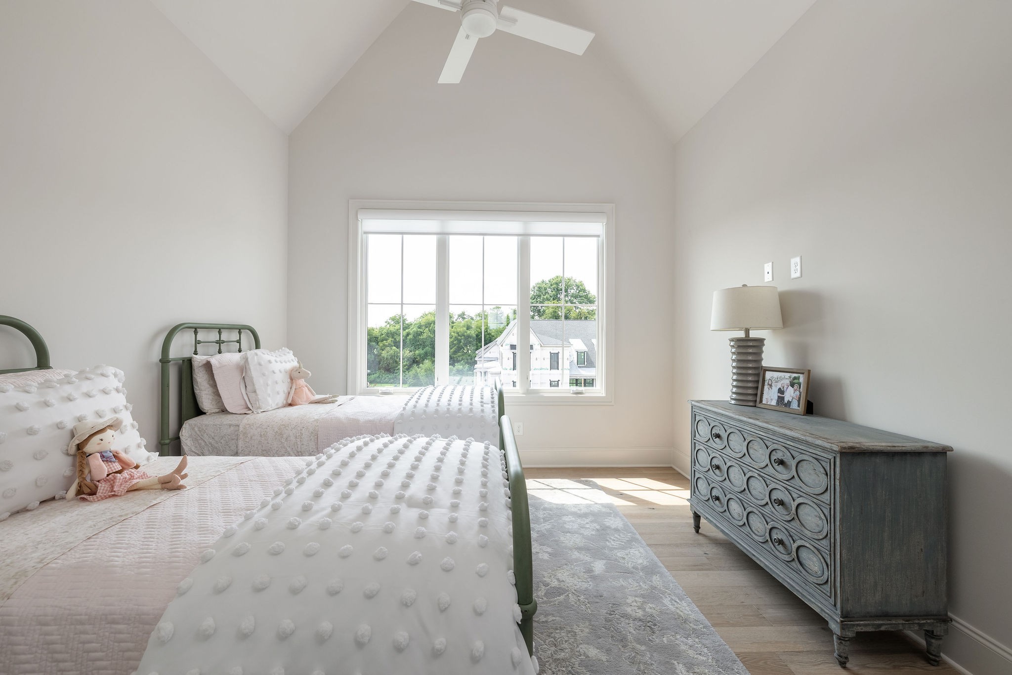 Twin bedroom with white textured bedding, green metal bed frames, and a large window overlooking trees.