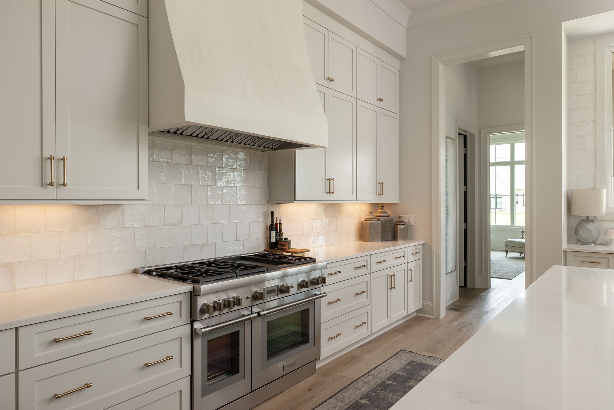 Bright white kitchen with brass cabinet pulls, tiled backsplash, and stainless steel double oven.