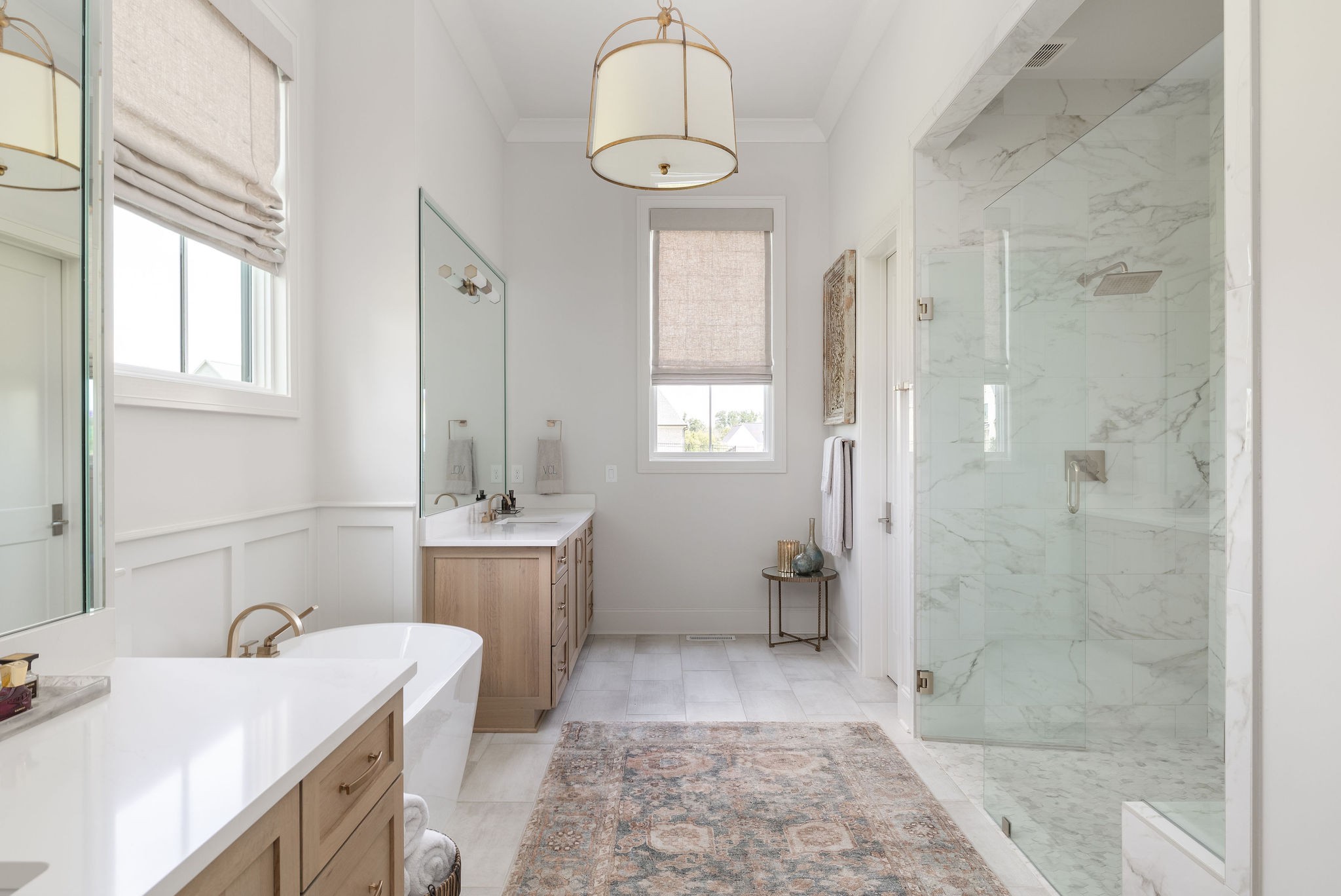 Primary bathroom with a freestanding tub, wood double vanity, and glass-enclosed marble shower.