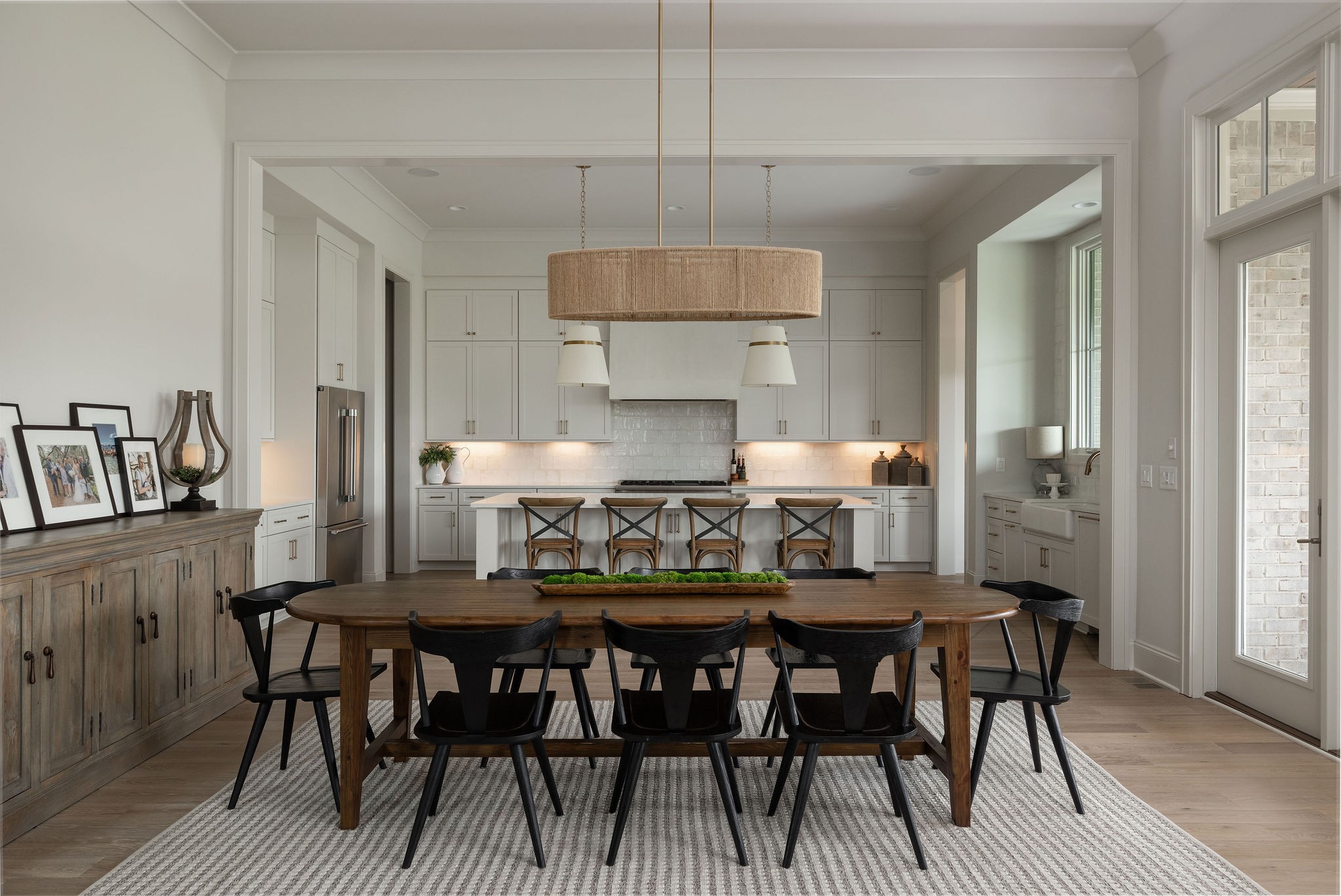 Dining table and dark chairs face a white kitchen with an island and four stools.