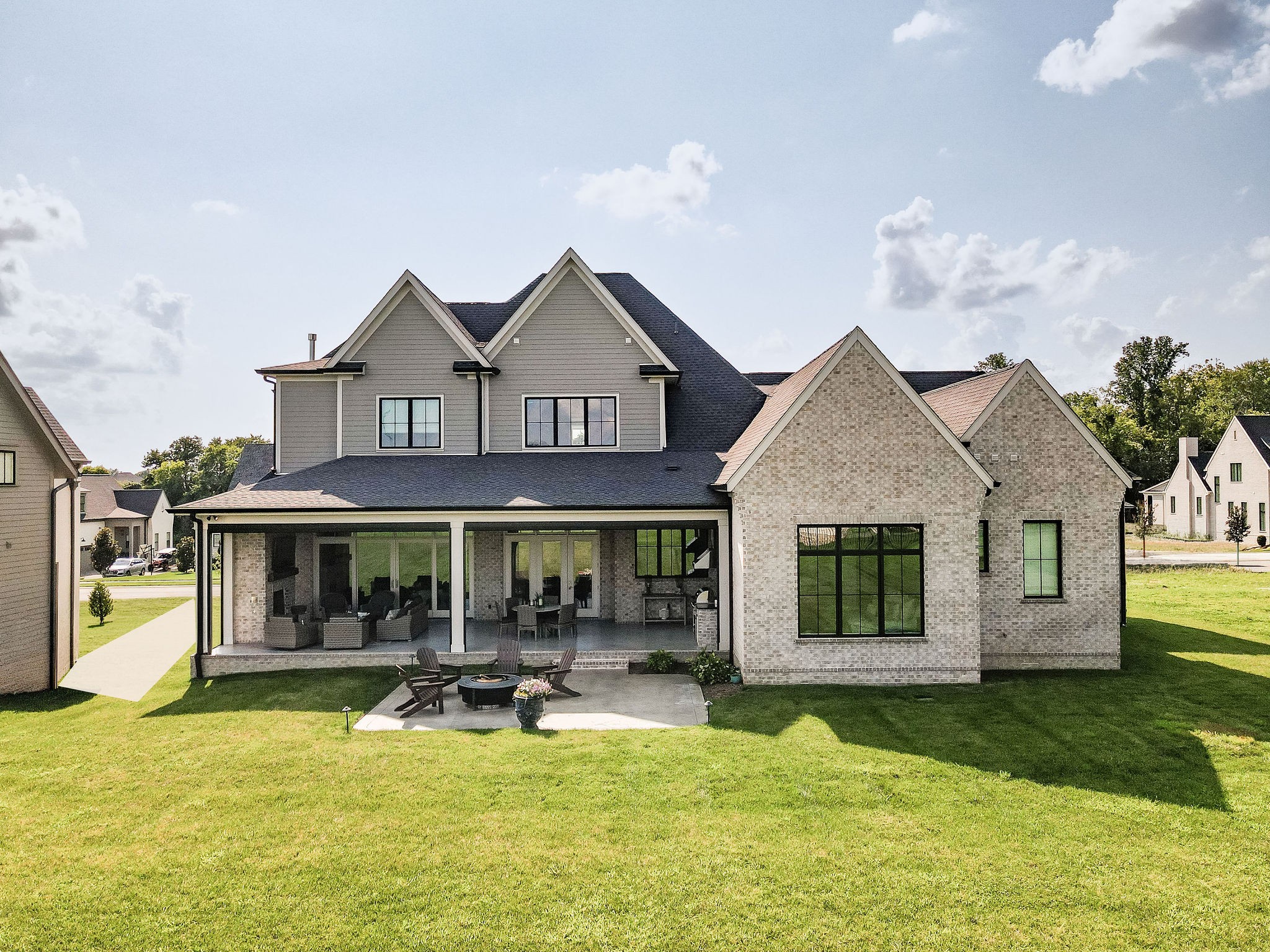 Rear of a two-story gray and brick home with a covered patio and outdoor fire pit seating.