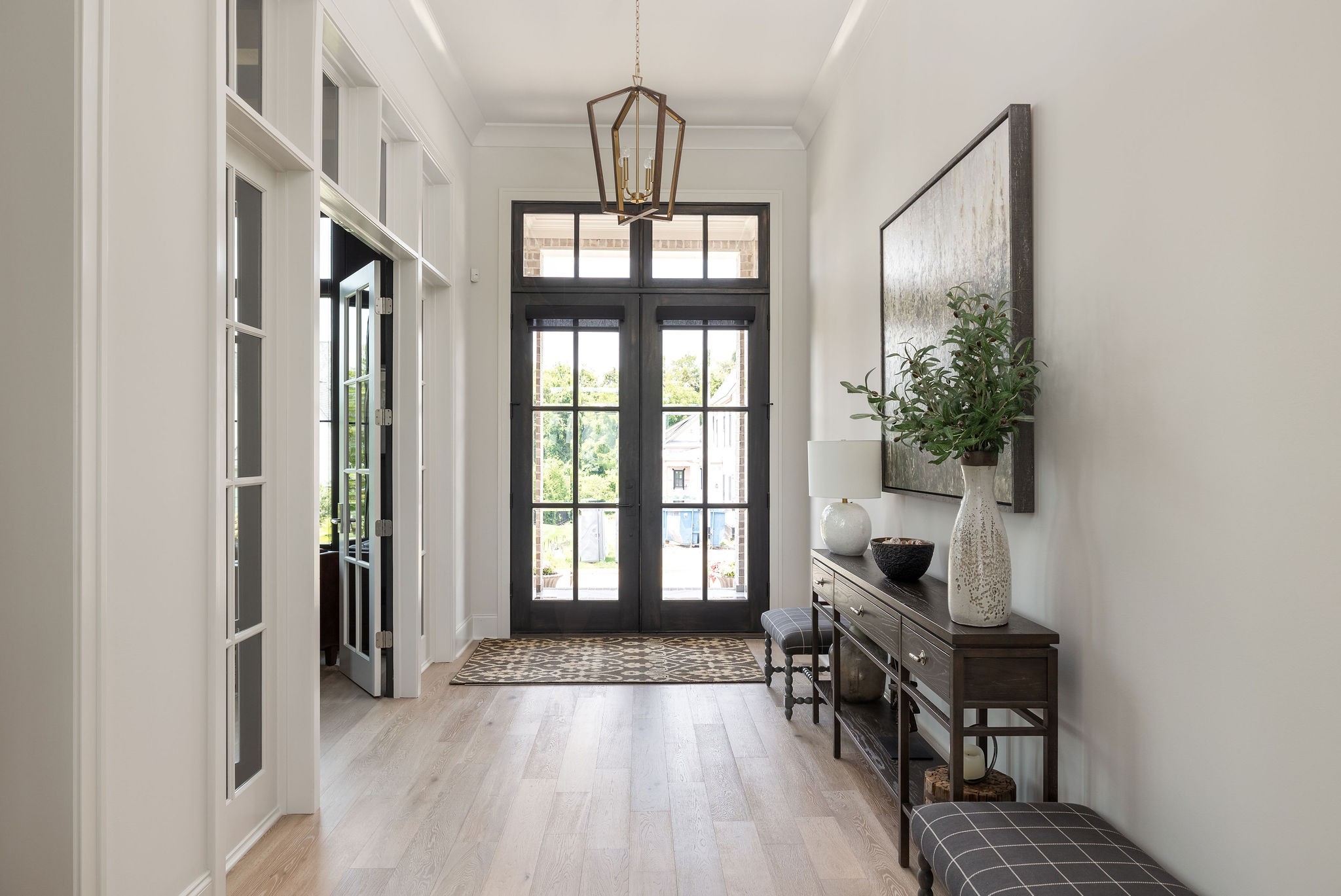 Furnished entry foyer with dark glass-paneled double doors, pale wood floors, and a console table.