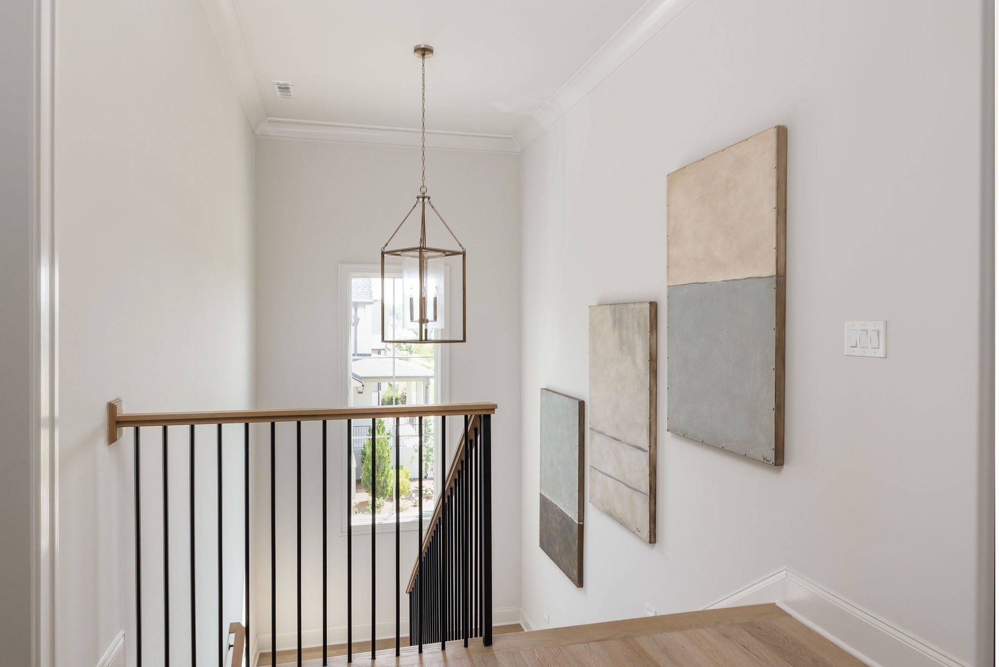 Upstairs stair landing with a black metal railing, hanging lantern, and abstract wall art.