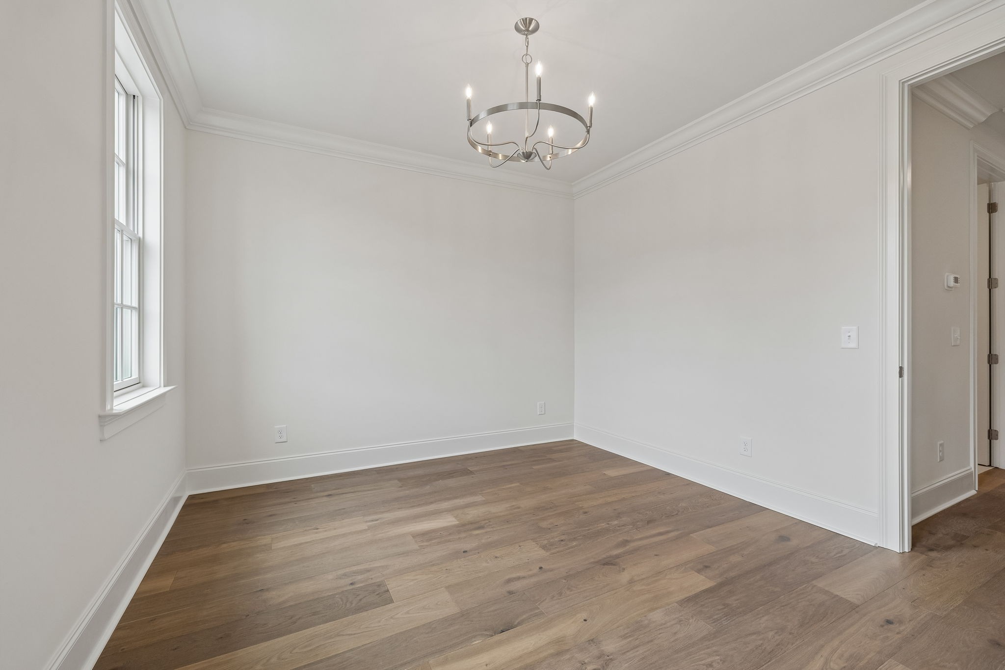 Empty dining room with wide-plank wood floors, a modern chandelier, and a tall window.