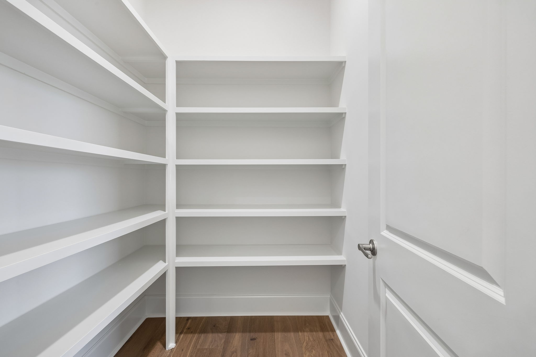 Walk-in pantry with white built-in shelves and a wood floor.