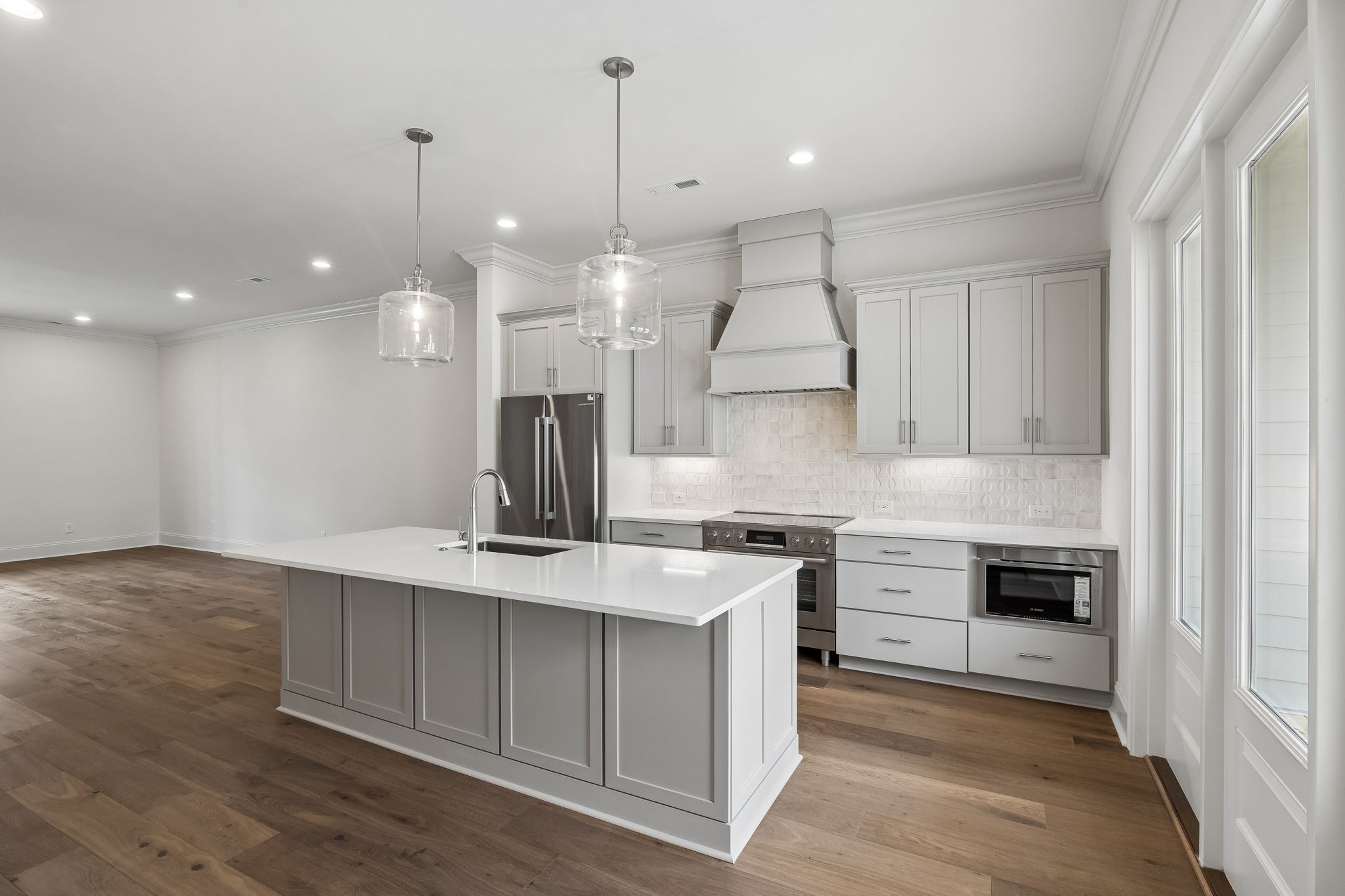 Kitchen with a large white island, stainless steel appliances, and warm wood floors.