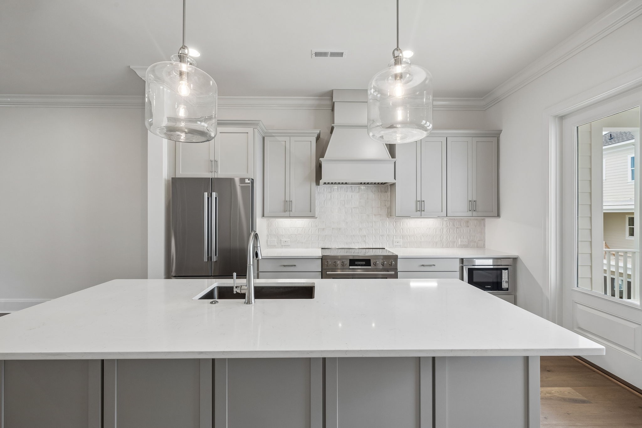 Modern kitchen with a large quartz island, glass pendant lights, and stainless steel appliances.