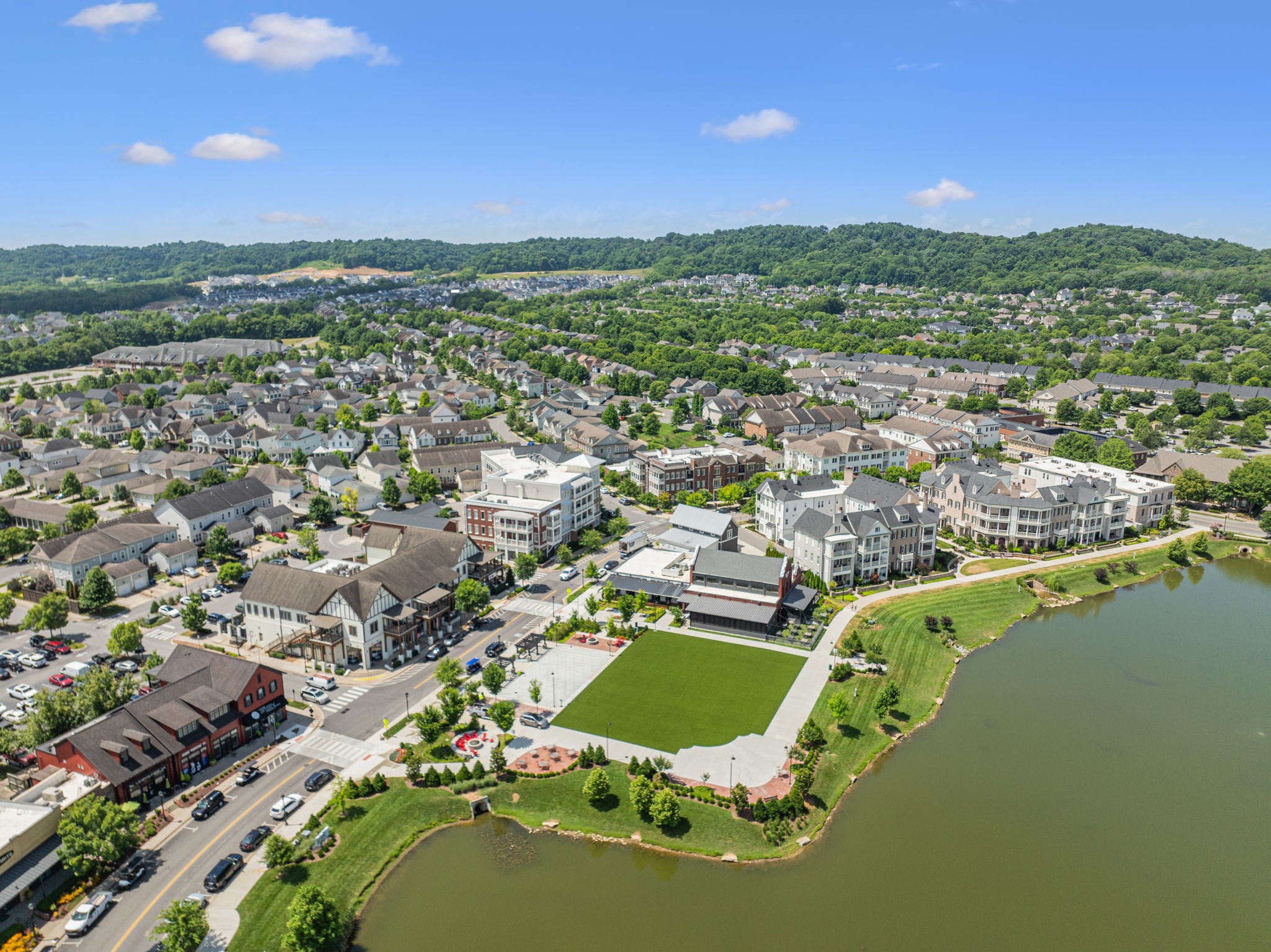 Aerial view of a lakeside town center with shops, homes, and wooded hills.