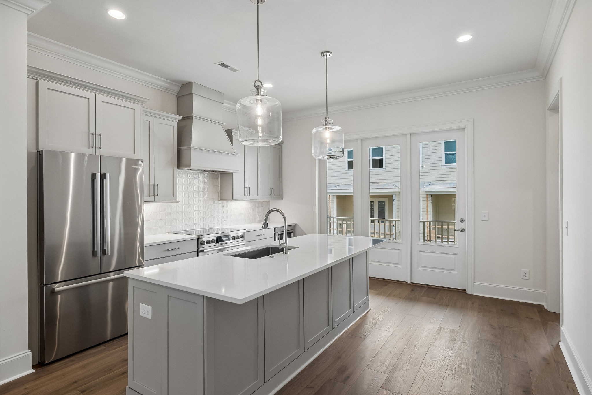 Modern kitchen with a large white island, gray cabinets, and stainless steel appliances.