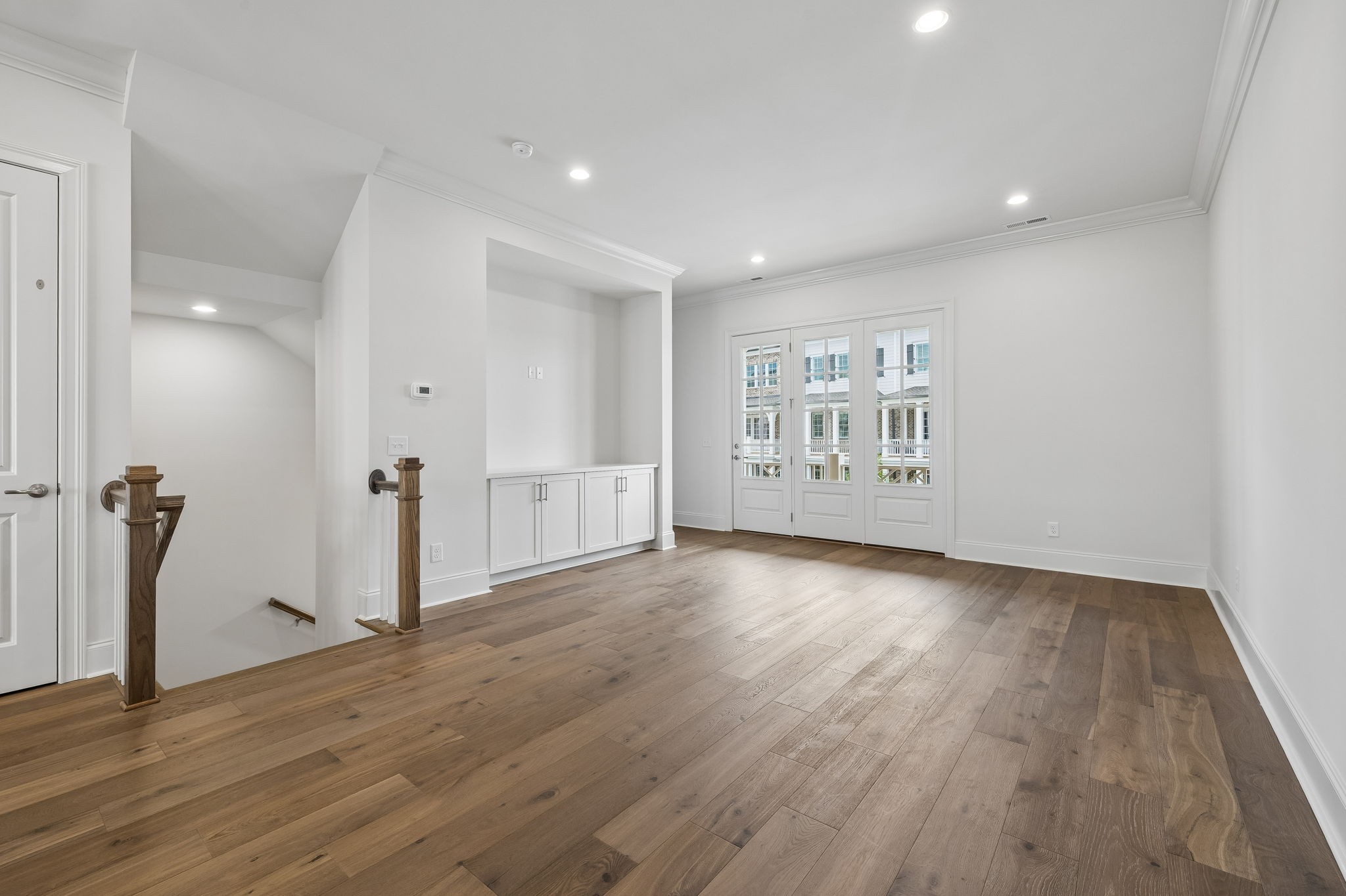 Empty upstairs room with wood flooring, built-in cabinets, and glass-paneled doors beside a stair opening.