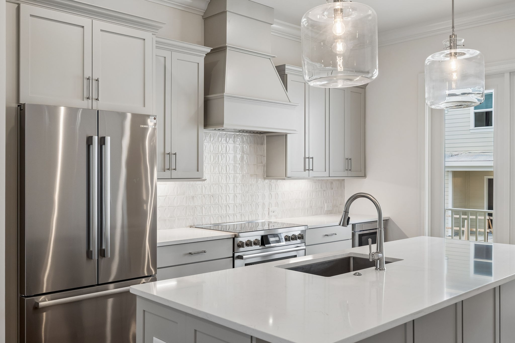 Modern kitchen with white cabinetry, patterned tile backsplash, stainless-steel appliances, and a large island.