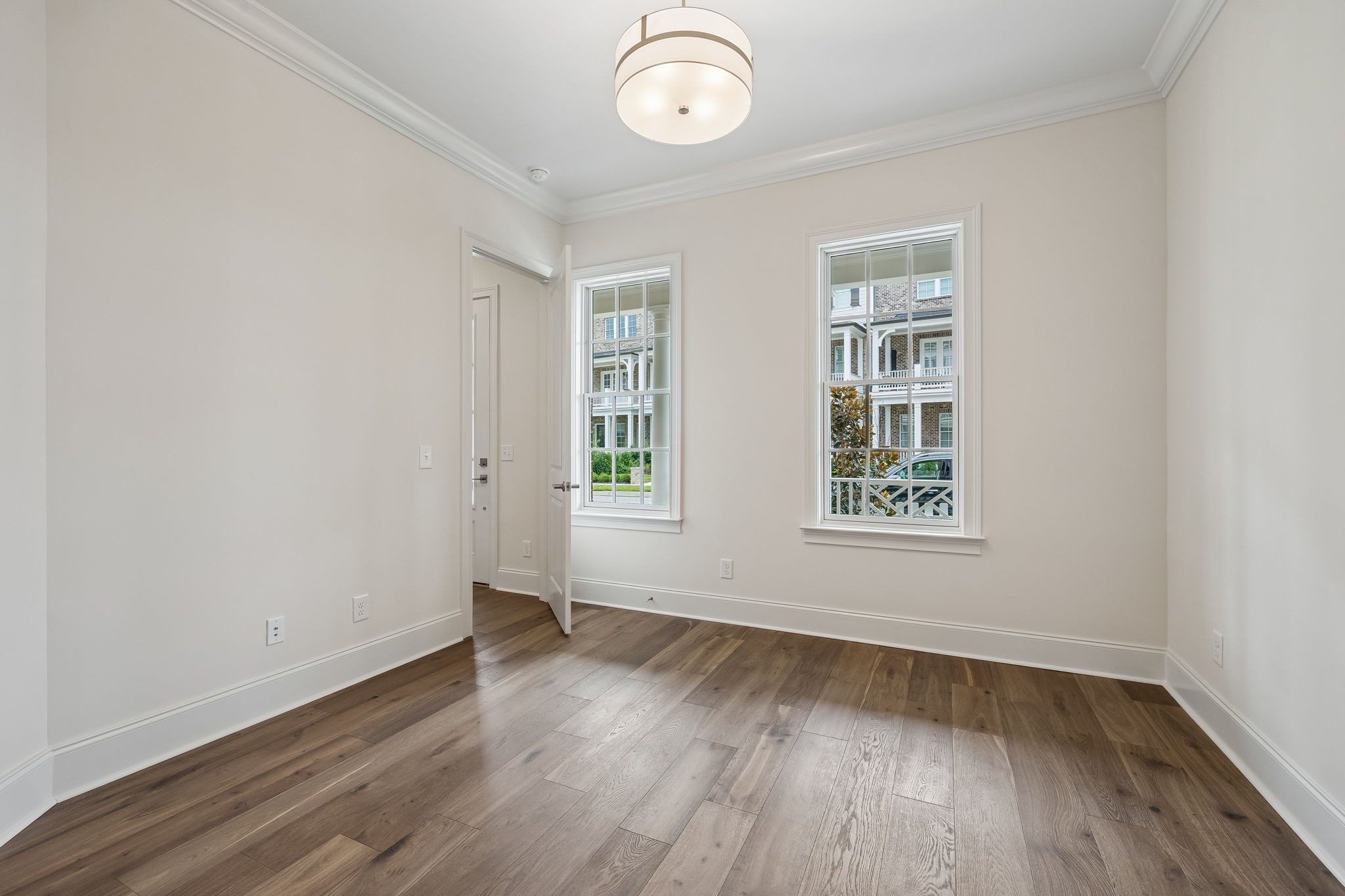 Empty room with wide-plank wood floors, two windows, and a round ceiling light.