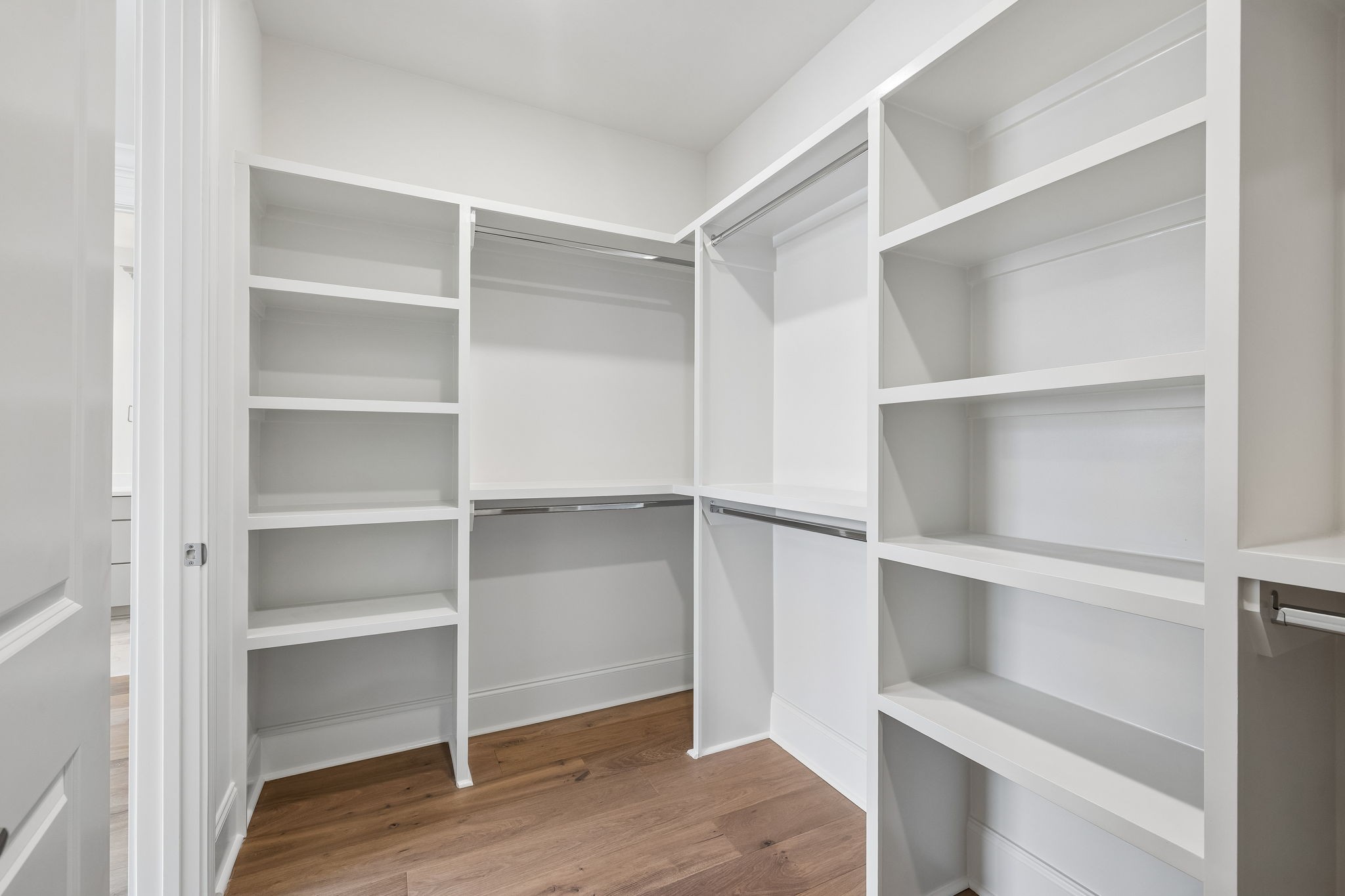 Walk-in closet with white built-in shelves, hanging rods, and wood flooring
