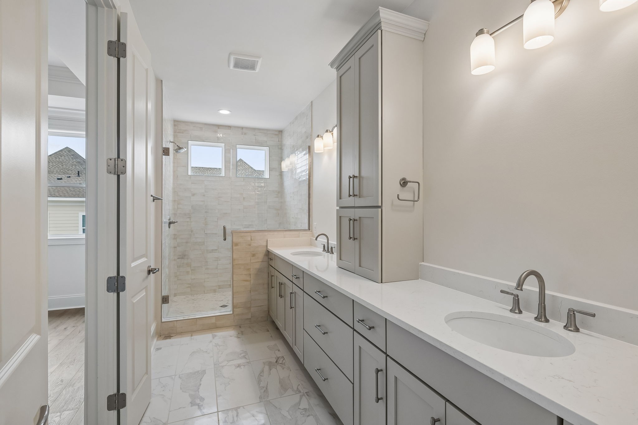 Bathroom with a long gray double vanity and a glass-enclosed shower with high windows.