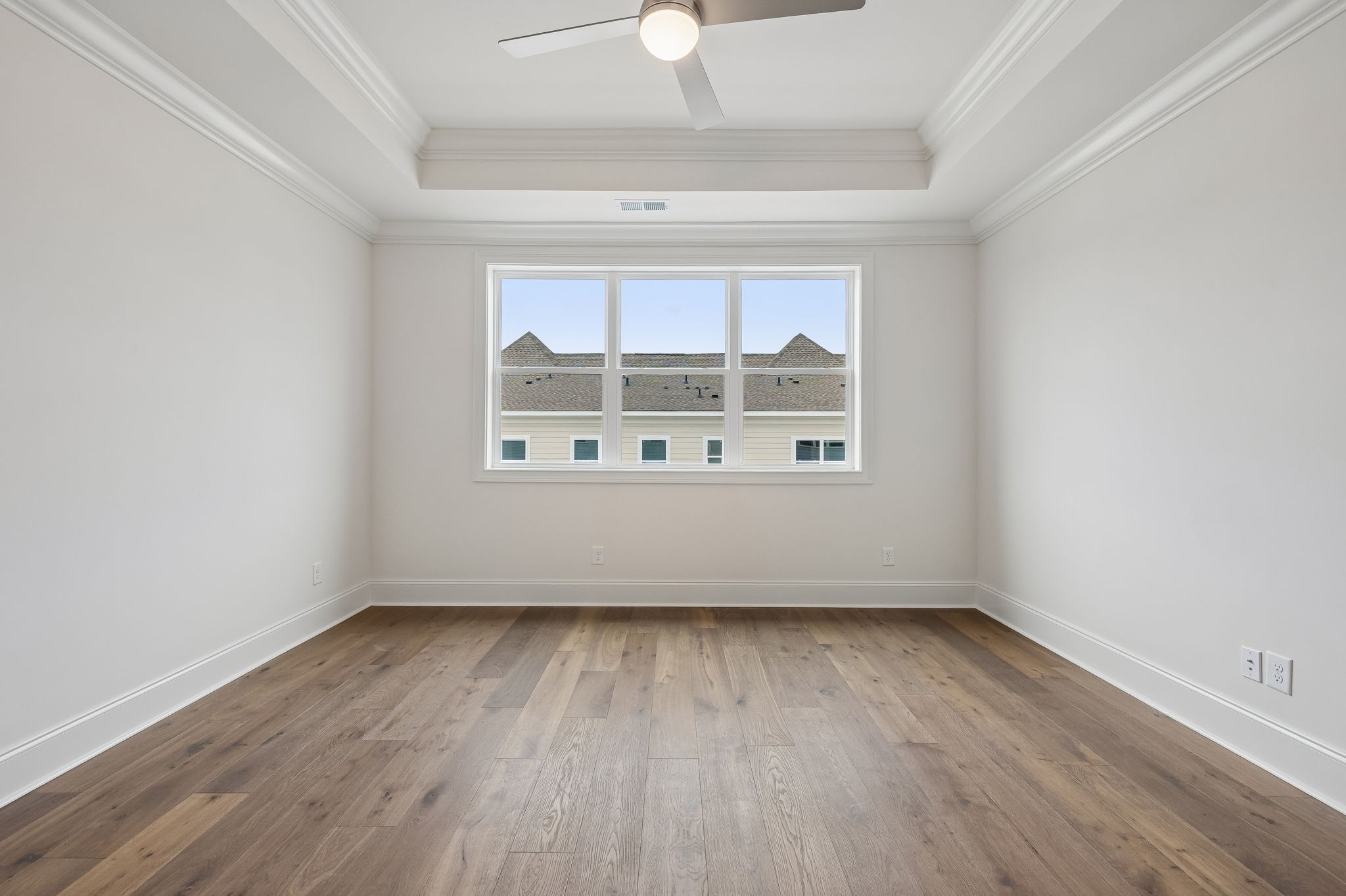Empty bedroom with wood flooring, tray ceiling, and a wide window.