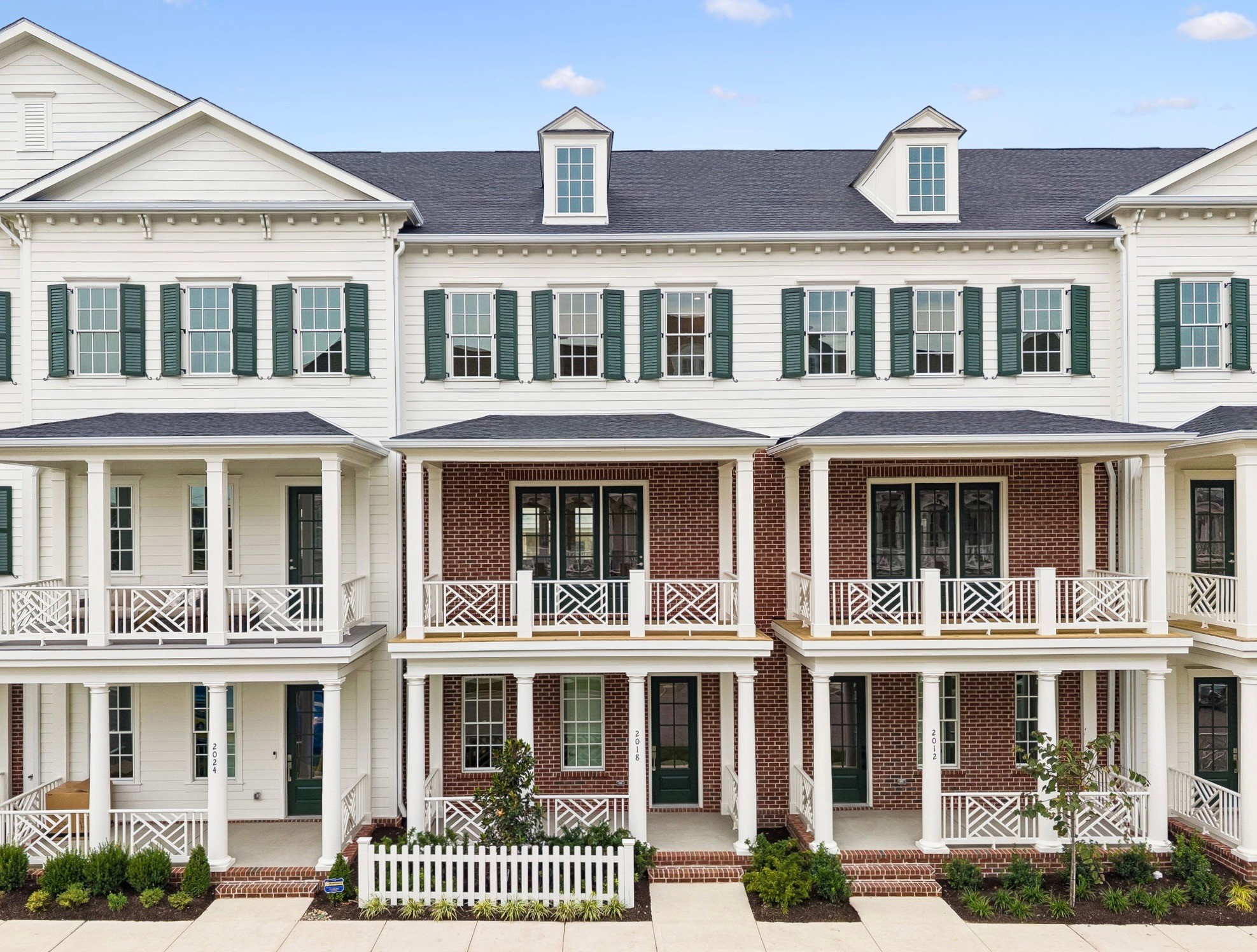 Attached townhomes with white porches and green shutters; central brick home marked 2018.