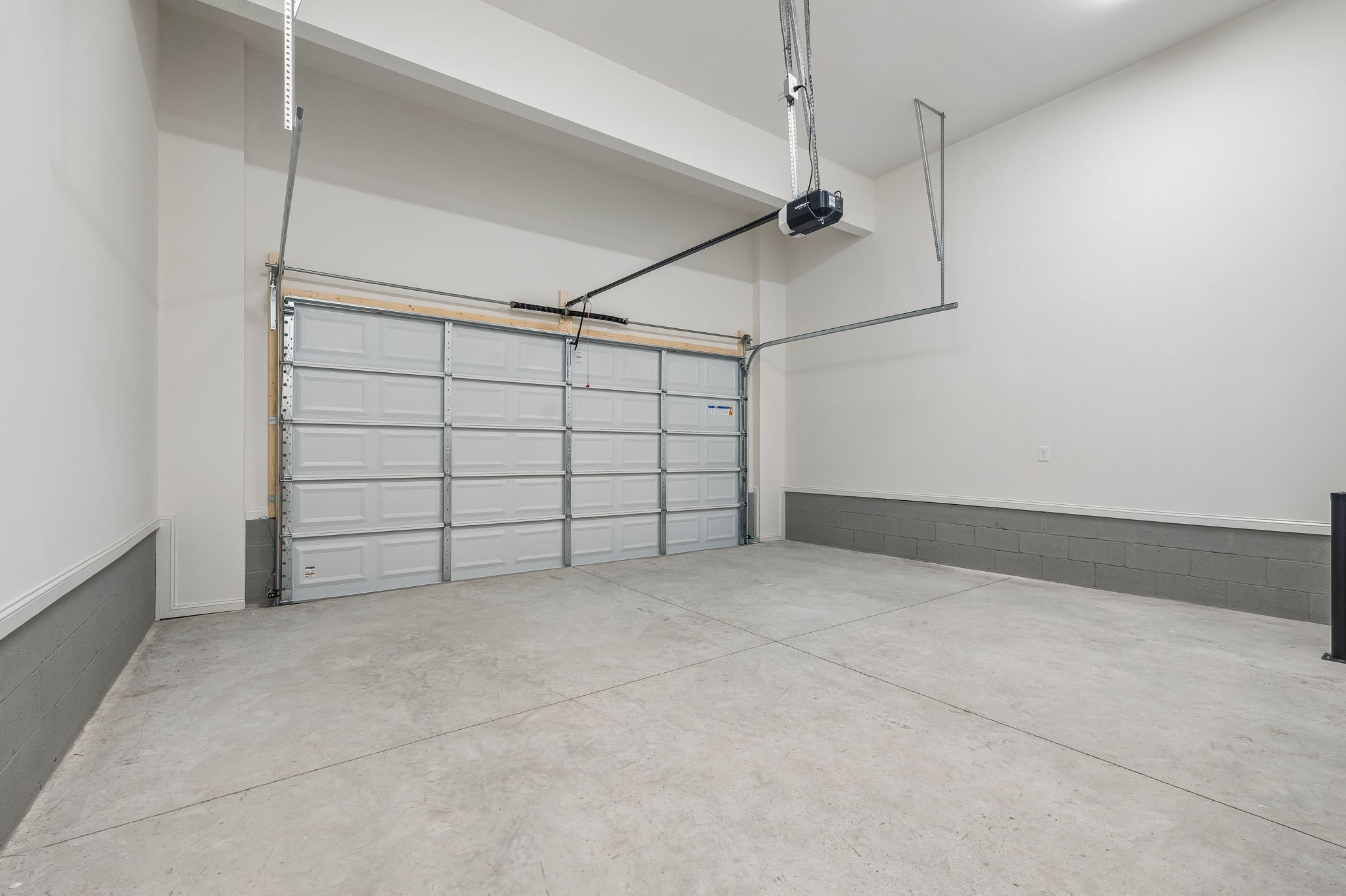 Empty garage with a wide sectional door, tall ceiling, and bare concrete floor.