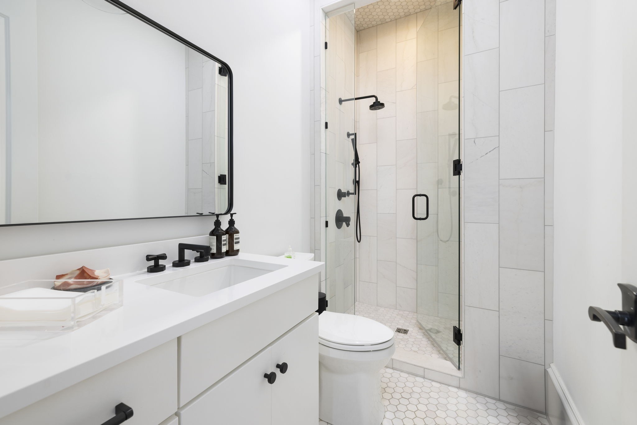 Modern bathroom with a white vanity, black-framed mirror, and glass shower with matte black fixtures.