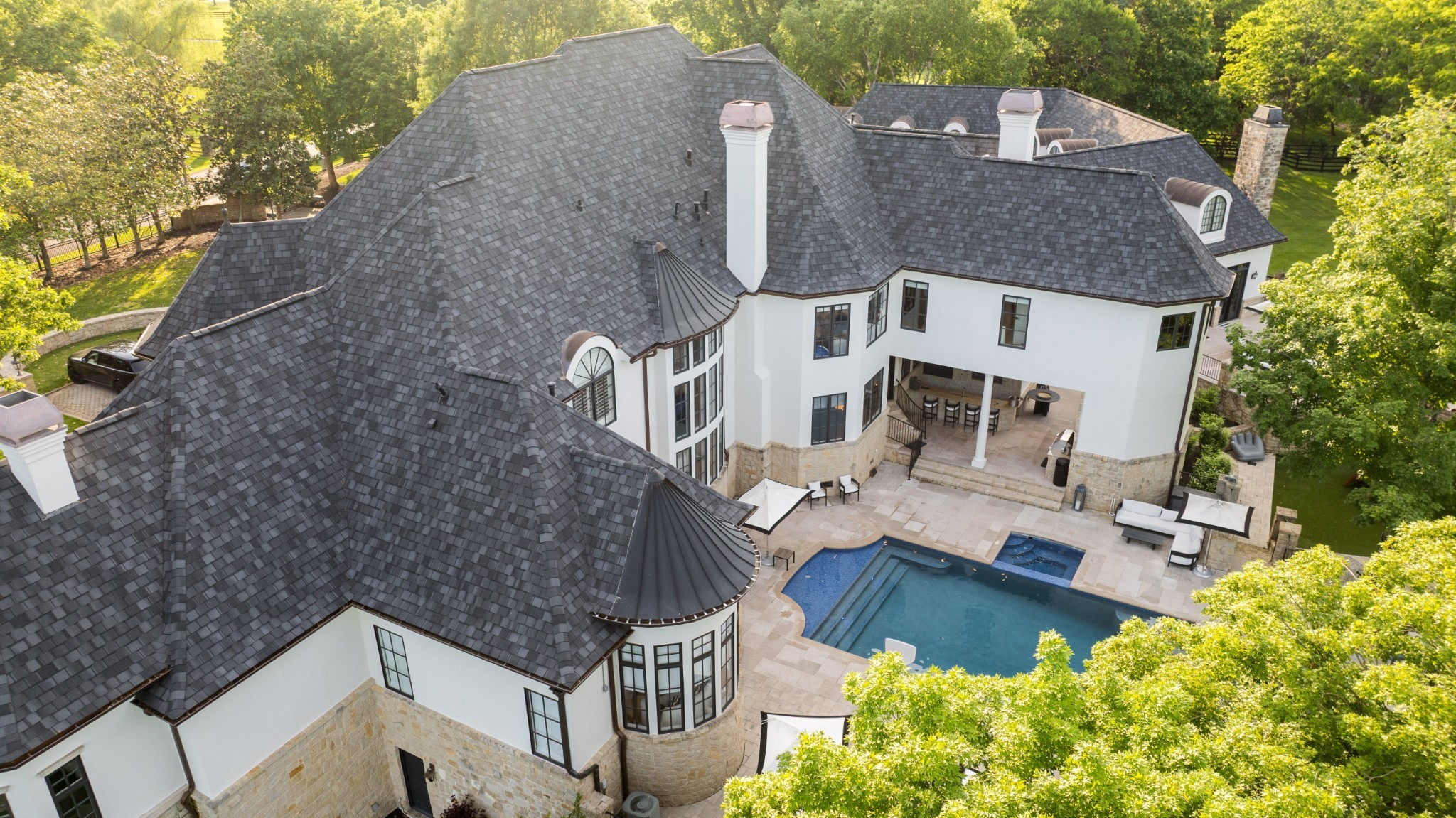 Aerial view of a large home with a dark roof, pool, and stone patio.