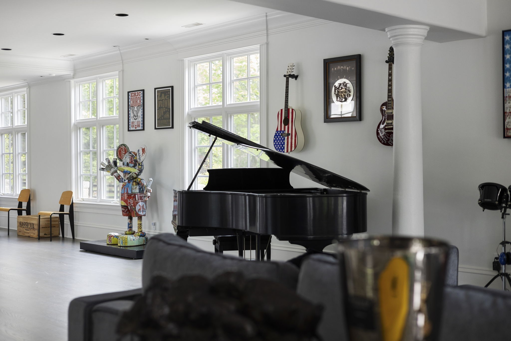 Music room with a grand piano, wall-mounted guitars, concert posters, and a colorful sculpture.