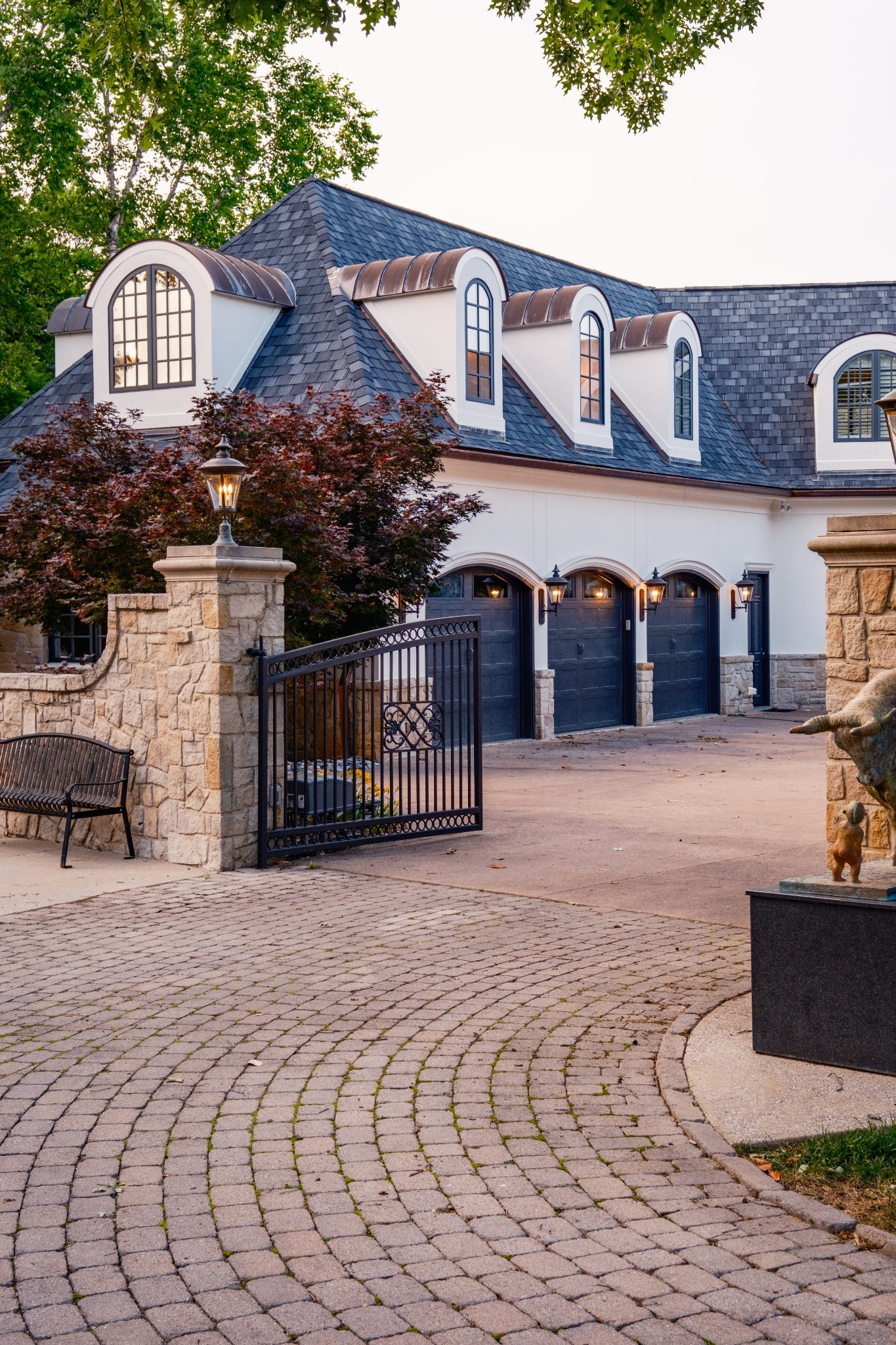House exterior with arched dormers, three garage doors, and a decorative metal driveway gate.