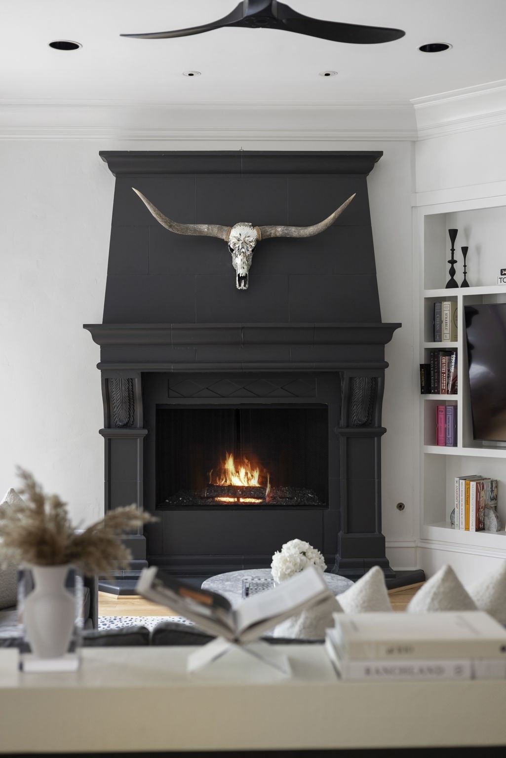Black living room fireplace with a burning fire and longhorn skull above the mantel.