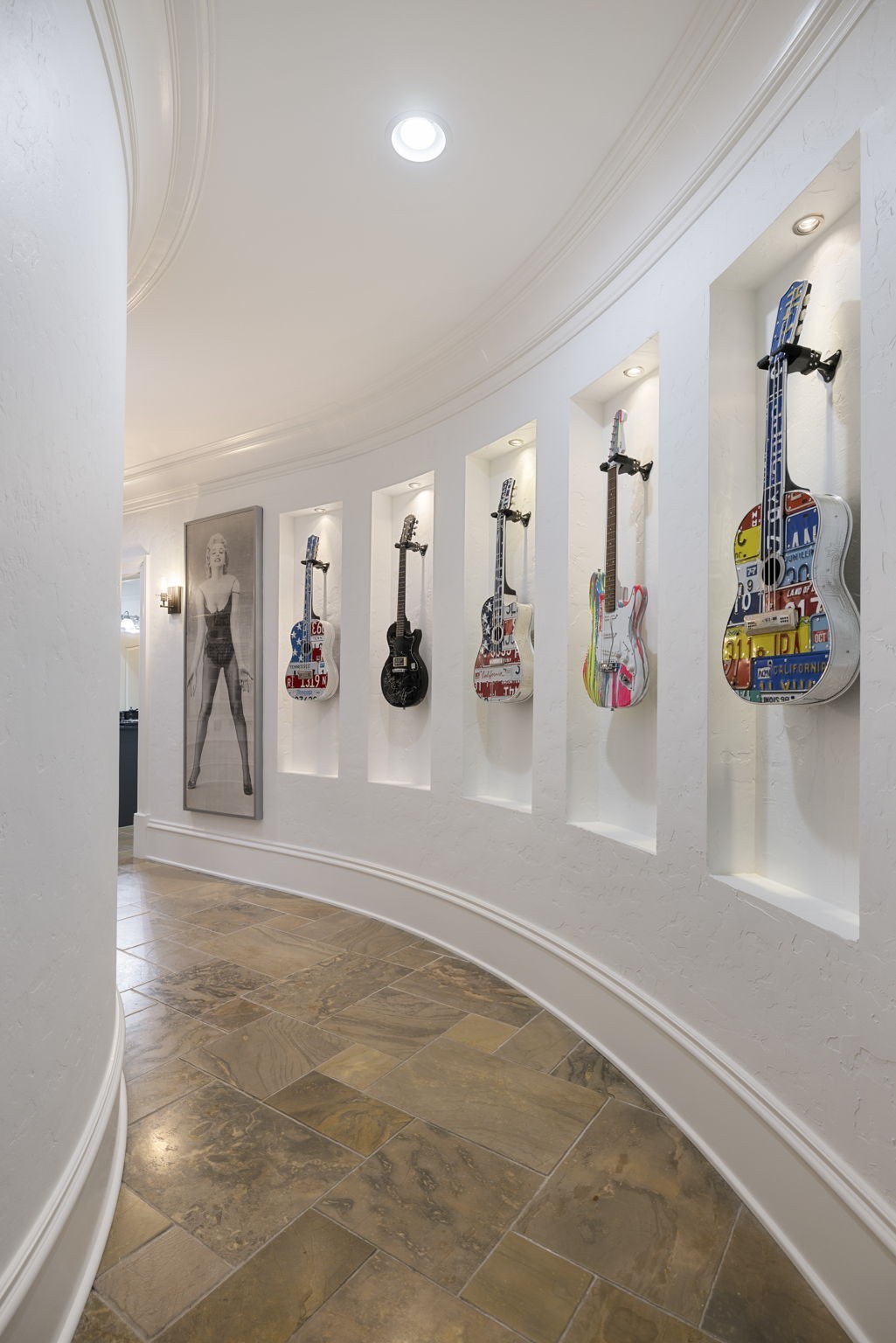 Curved hallway with stone tile floors and guitars displayed in illuminated wall niches.