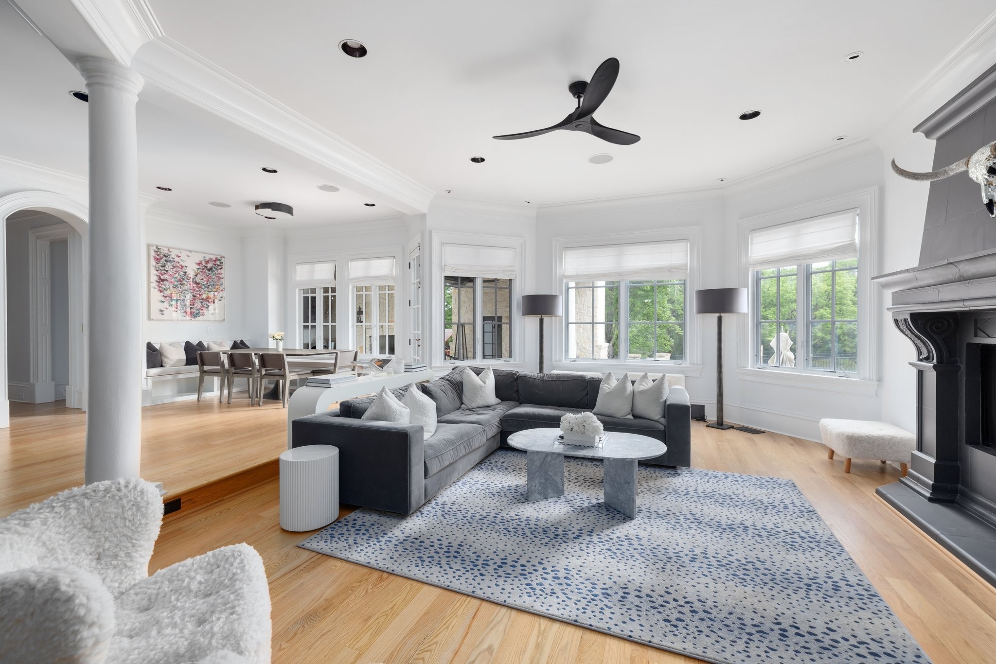 Living room with a gray sectional, patterned rug, large windows, and fireplace.