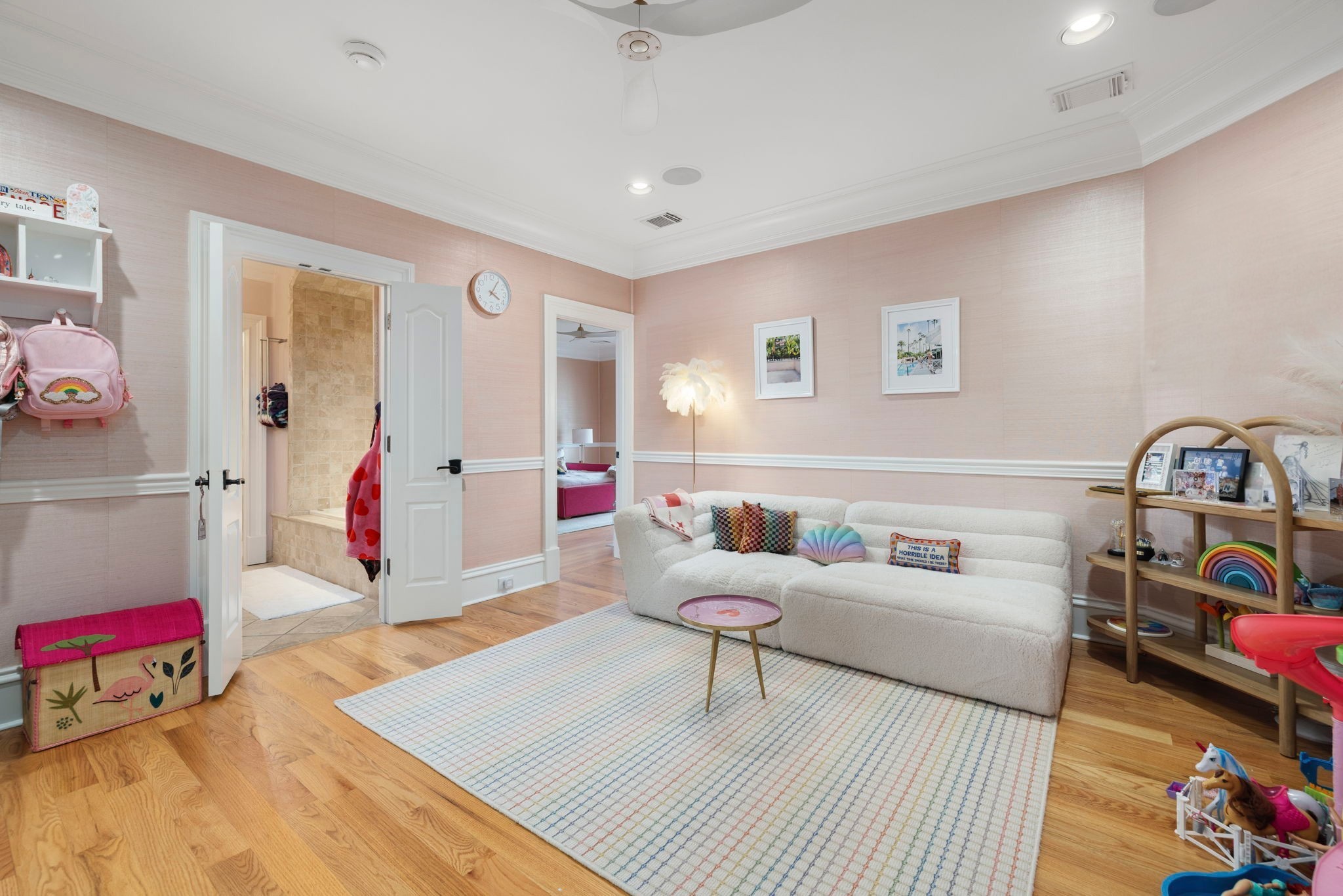 Children’s sitting room with a white sofa, pink walls, toys, and open doors to adjoining rooms.