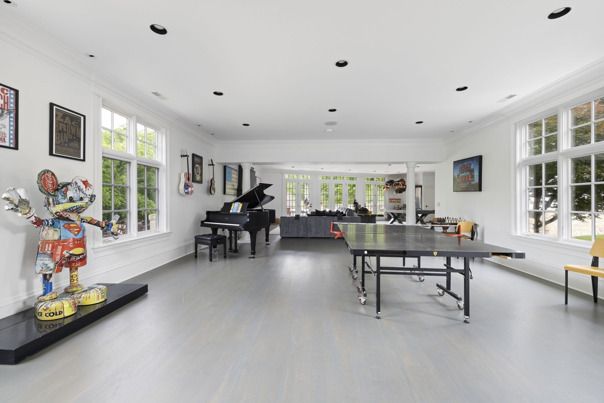 Bright recreation room with a ping-pong table, grand piano, large windows, and colorful sculptural figure.