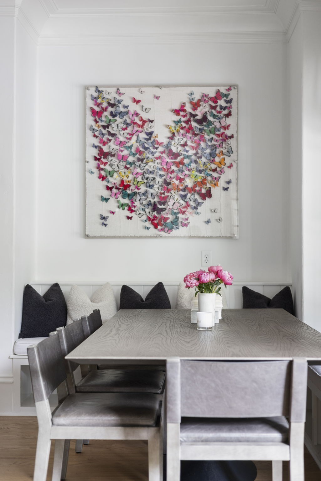 Dining area with a gray wood table, cushioned bench, and colorful butterfly artwork.