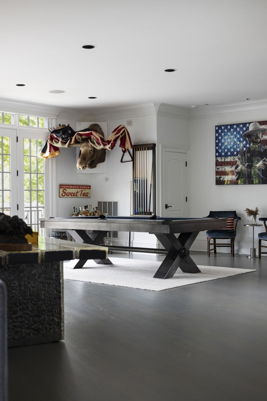 Game room with a billiards table, tall windows, pool cues, and patriotic decor.
