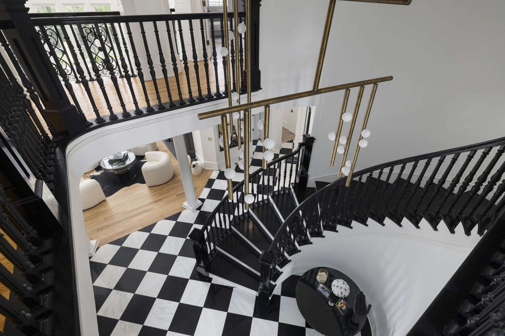 Grand foyer with sweeping black staircases, checkerboard floor, and brass pendant lights.
