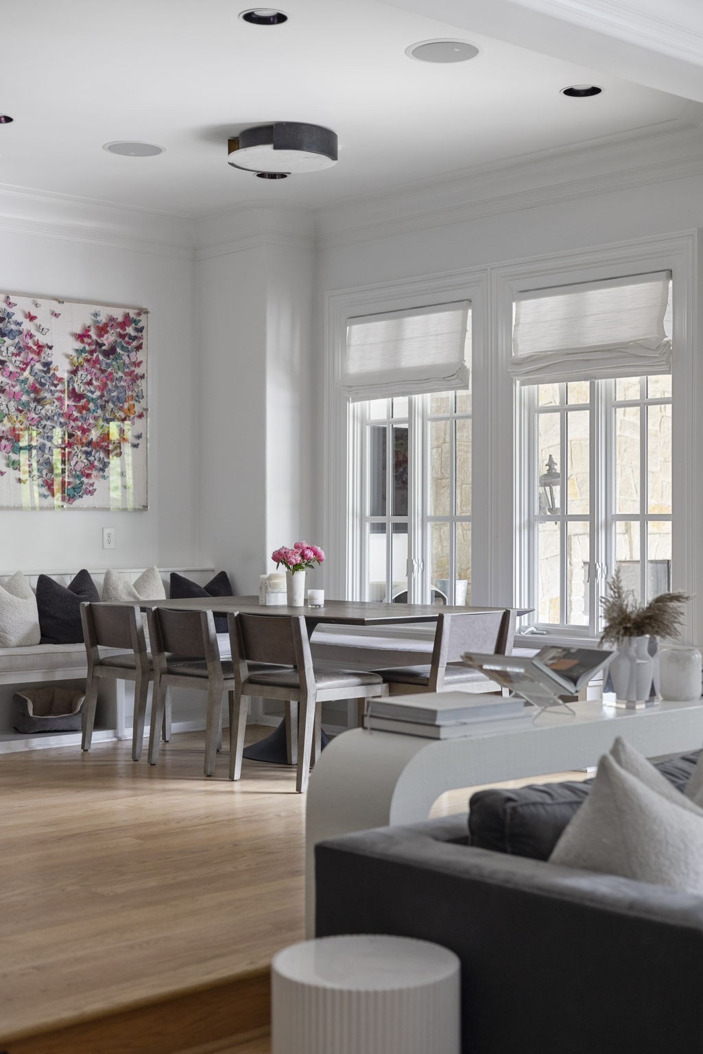 Dining area with a dark wood table, window-side banquette, and tall windows with white shades.