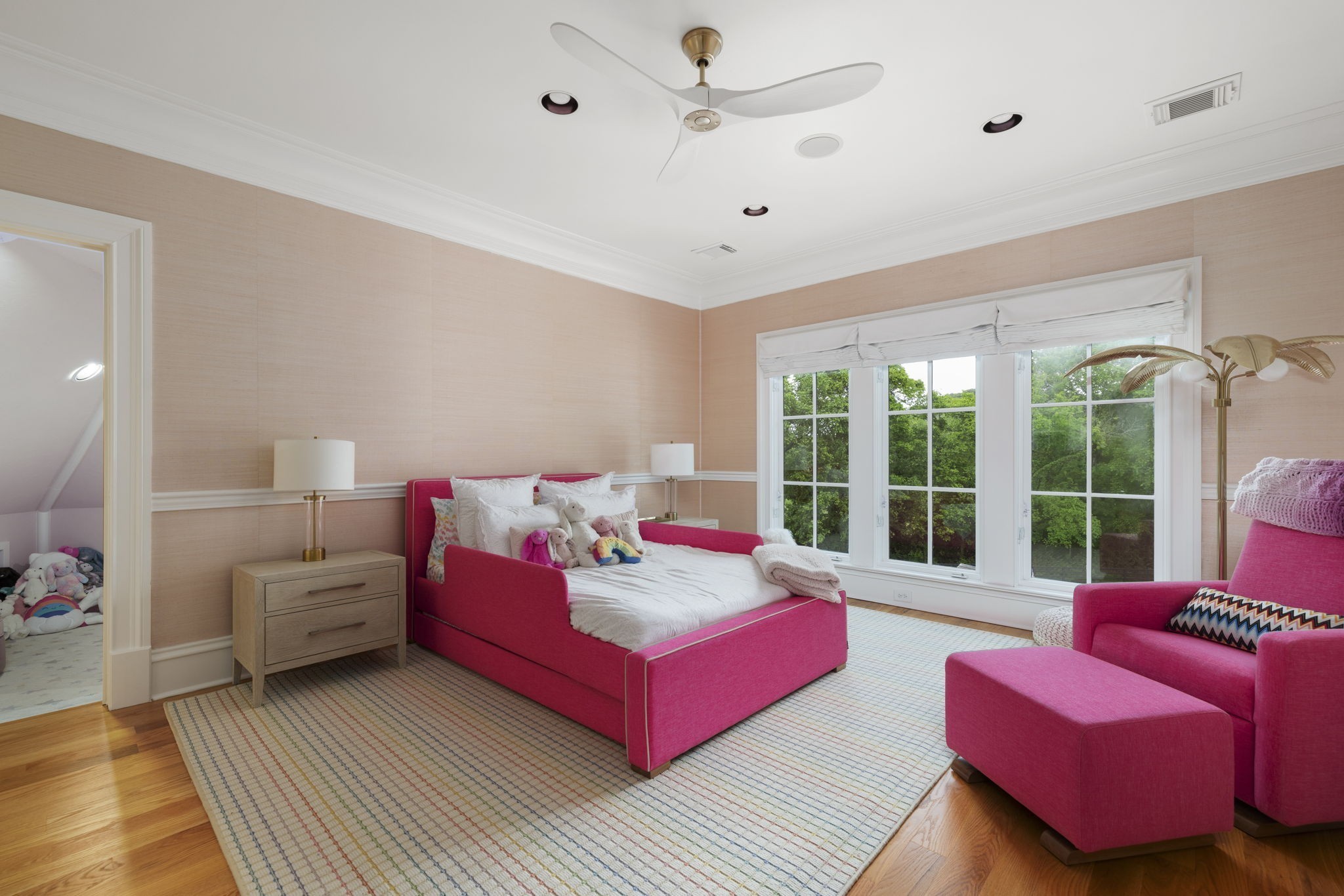 Bedroom with a bright pink bed and armchair beside large windows overlooking trees.