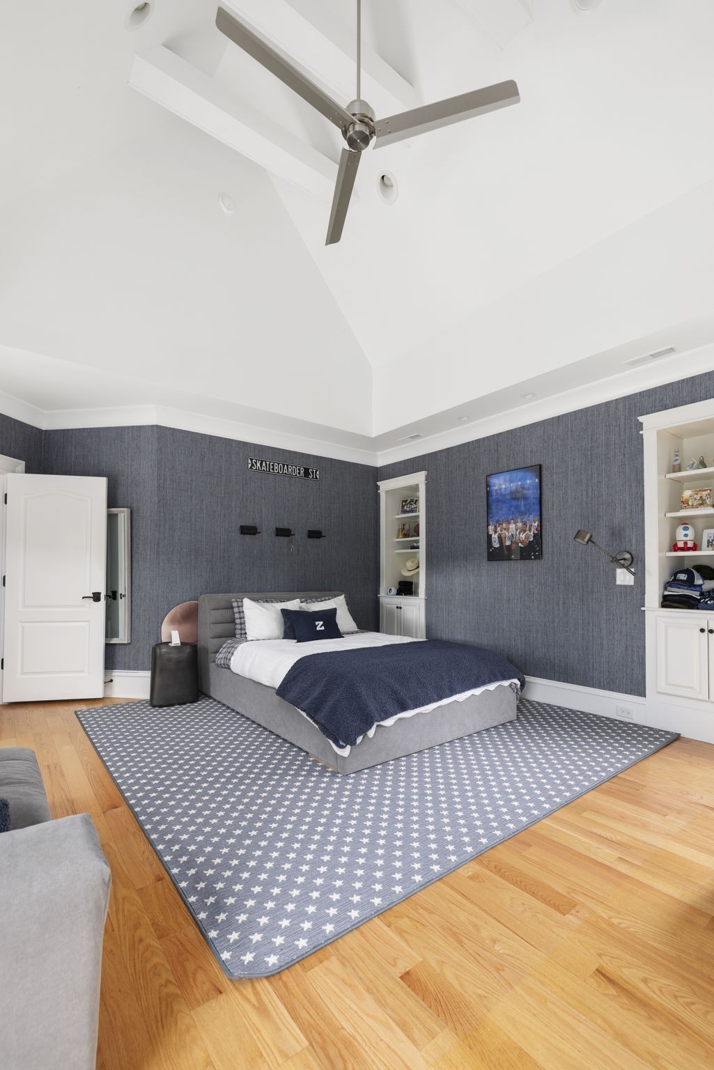 Bedroom with a vaulted ceiling, gray bed, navy bedding, and a star-patterned rug.