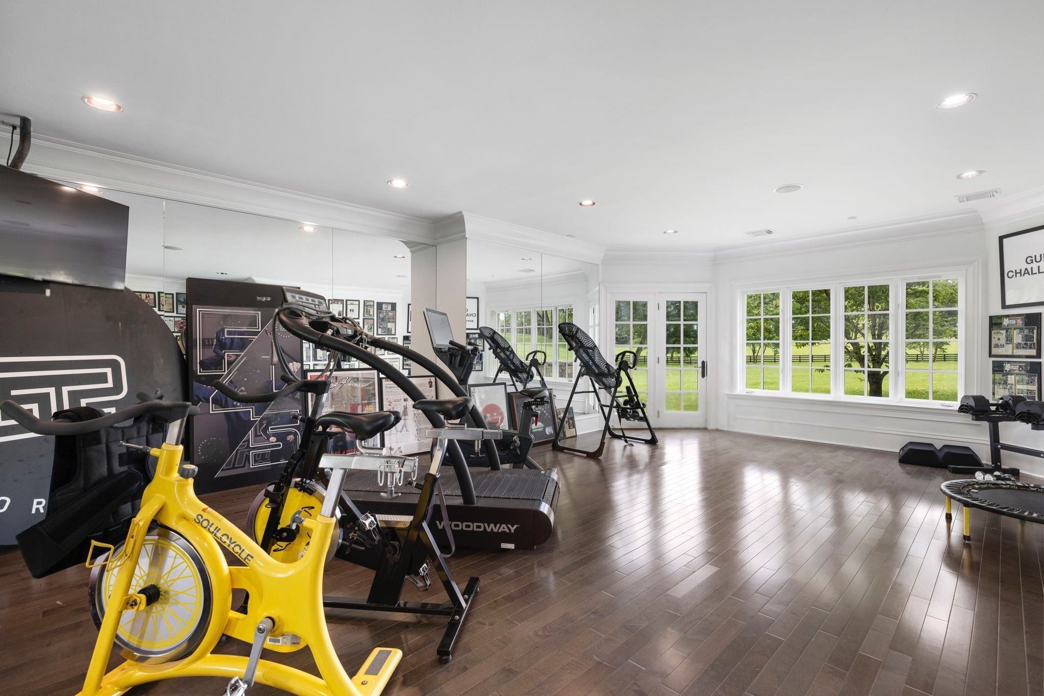 Home gym with a yellow stationary bike, treadmills, and large windows overlooking a green lawn.