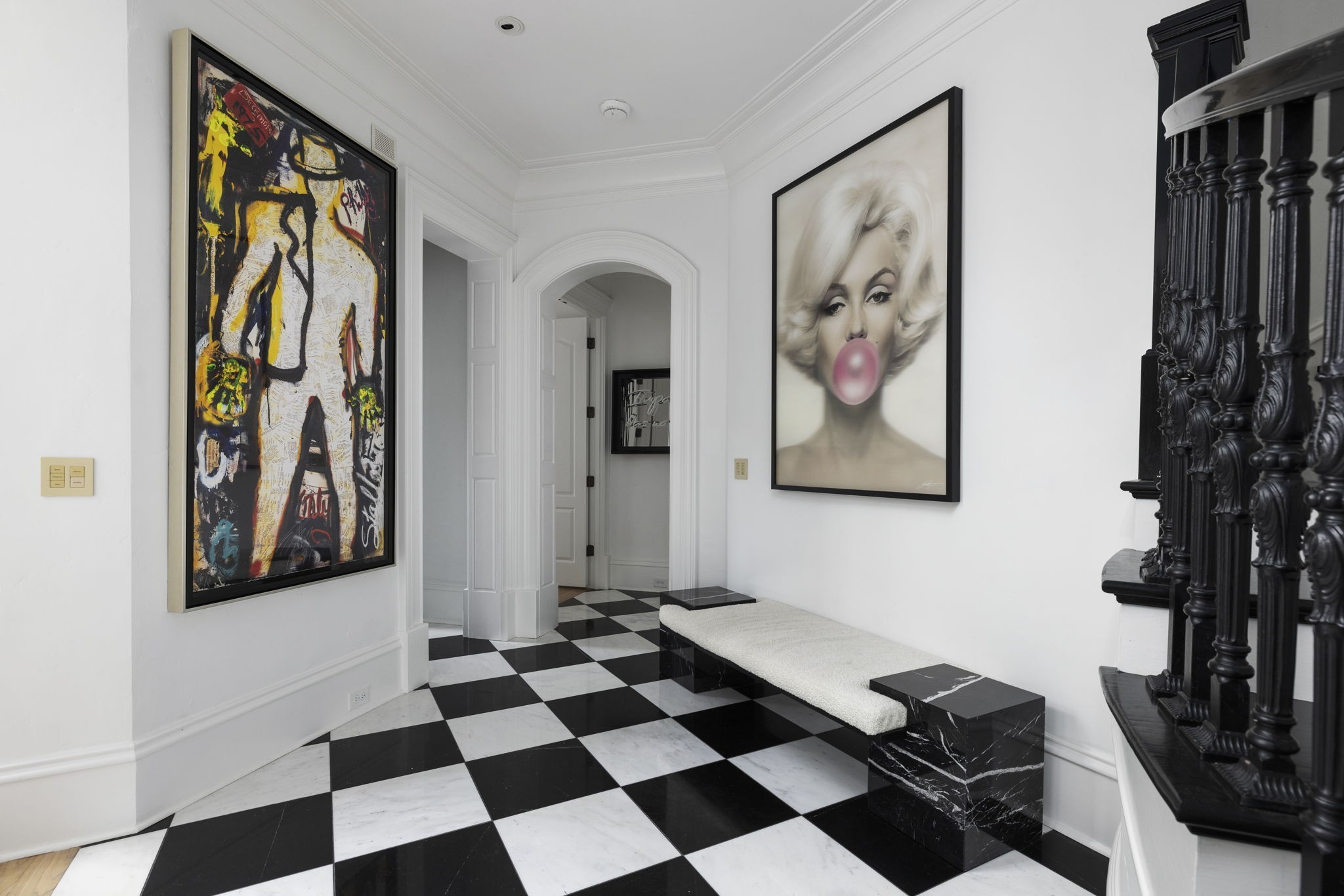 Foyer with a checkerboard floor, framed artwork, marble bench, and ornate dark staircase railing.