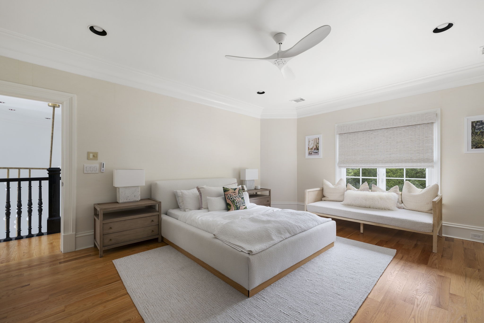 Furnished bedroom with an upholstered bed, hardwood floors, and a cushioned bench beneath the window.