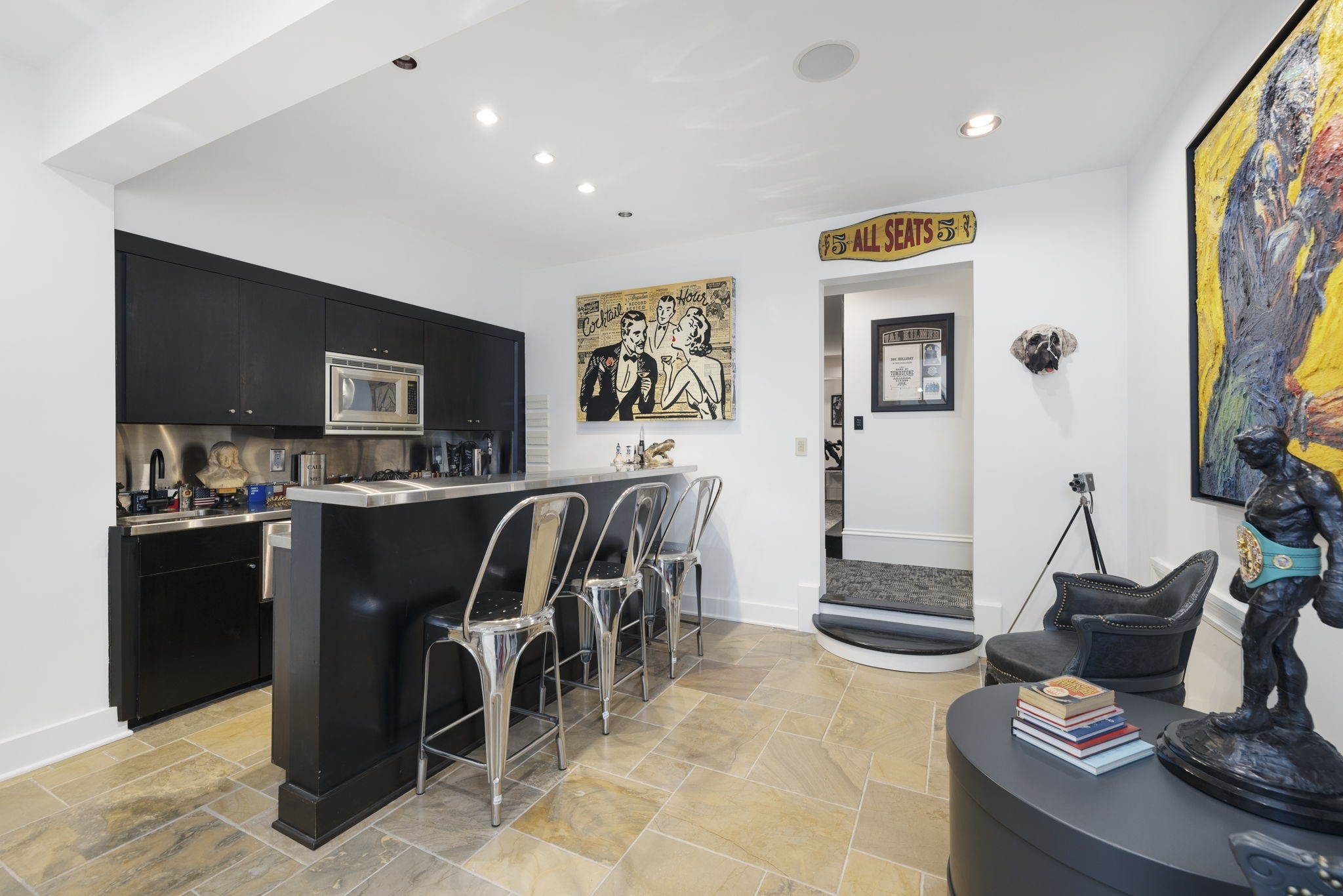 Interior bar with black cabinetry, stainless-steel counter, metal stools, and vintage-style wall art.