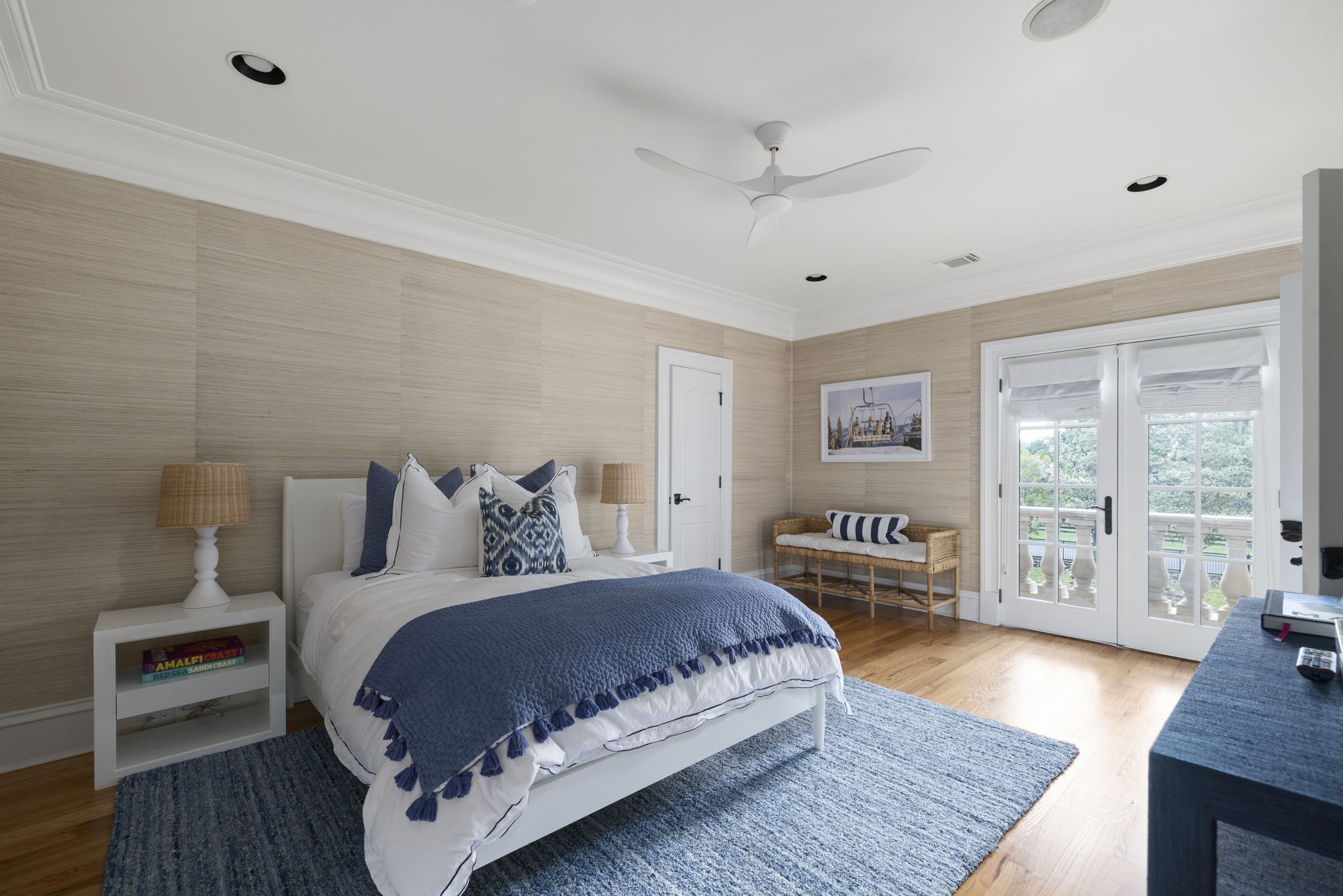 Bedroom with blue-and-white bedding, woven beige walls, and French doors opening to a balcony.