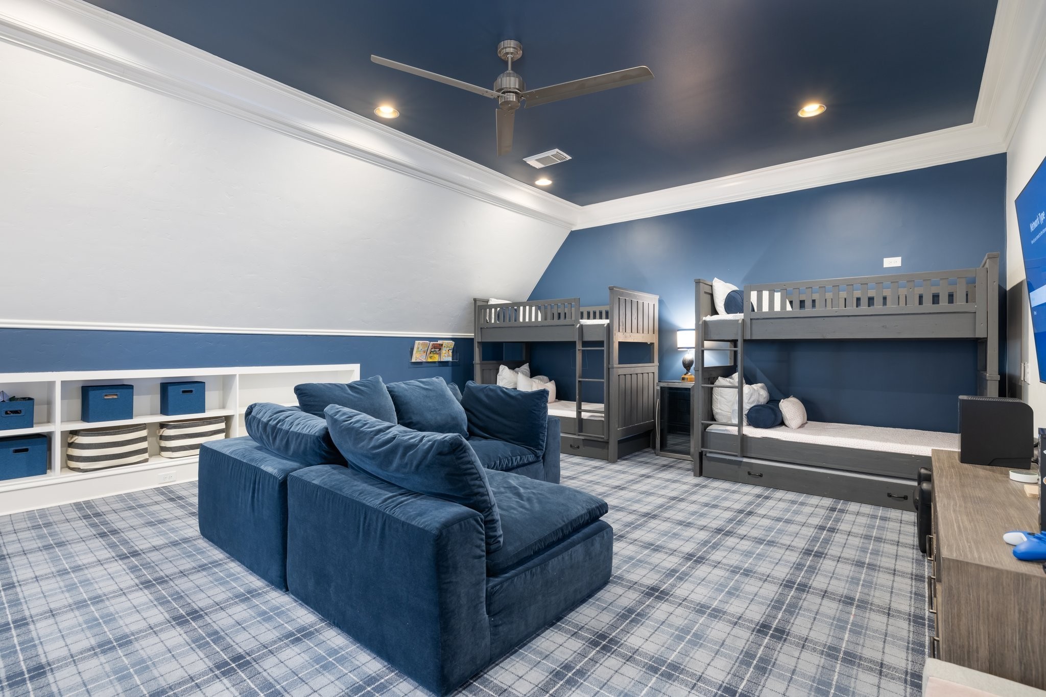 Bedroom with gray bunk beds, a navy sectional sofa, and blue-and-white plaid carpet.