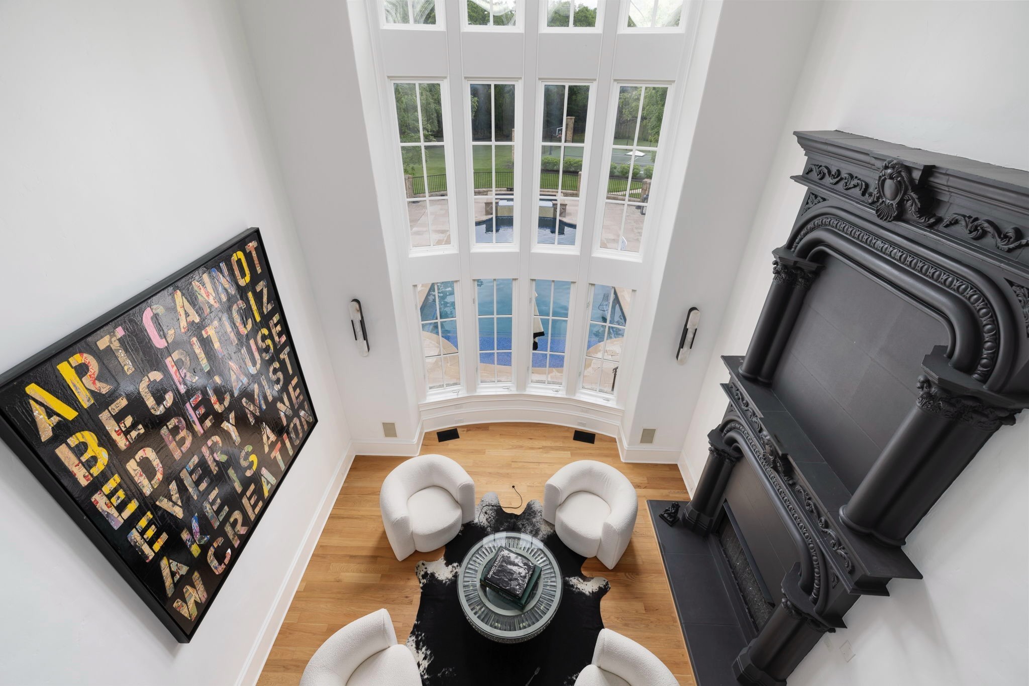 Furnished sitting area with an ornate black fireplace and tall windows overlooking a swimming pool.