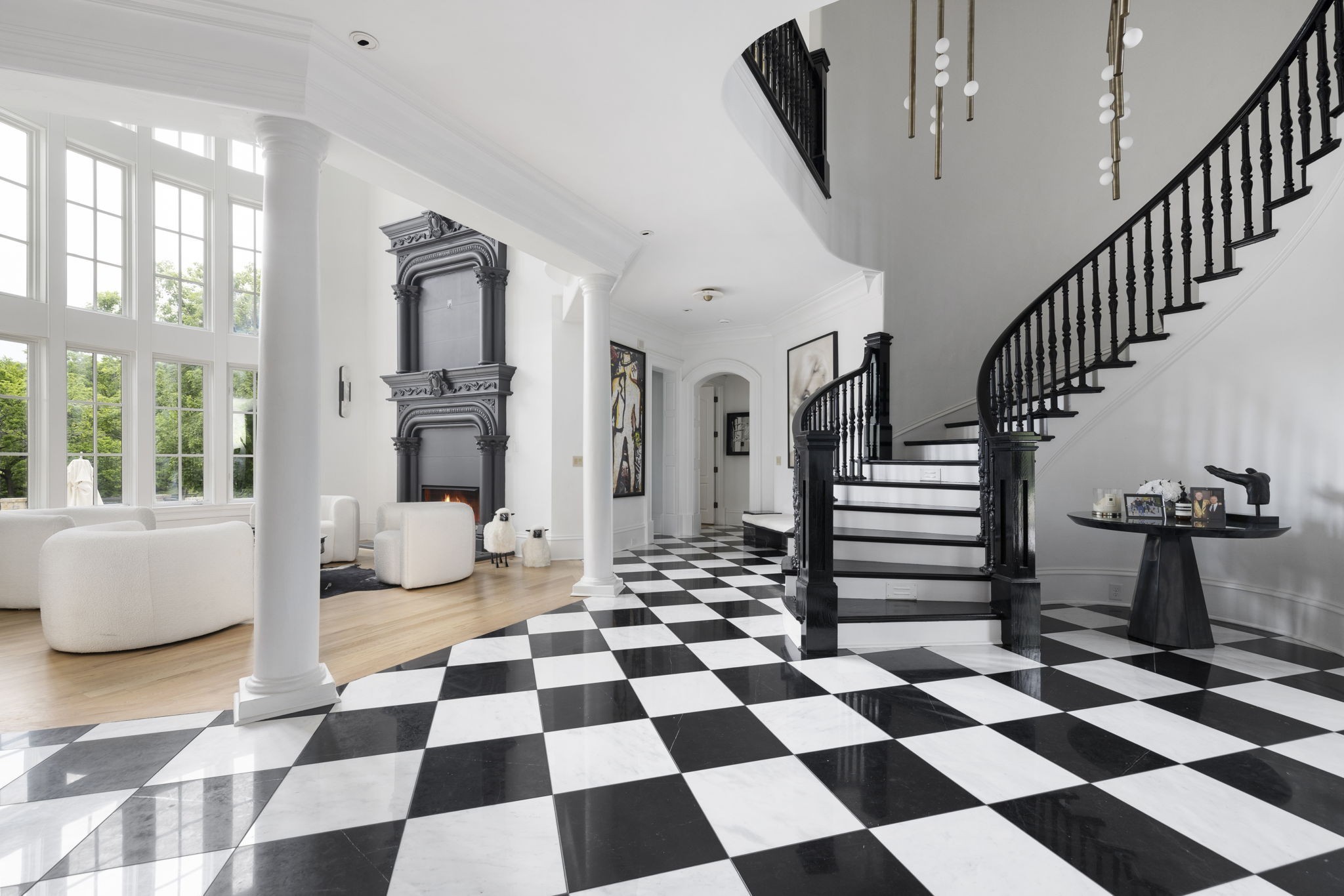 Foyer with a sweeping black staircase, checkerboard floor, tall windows, and ornate fireplace.
