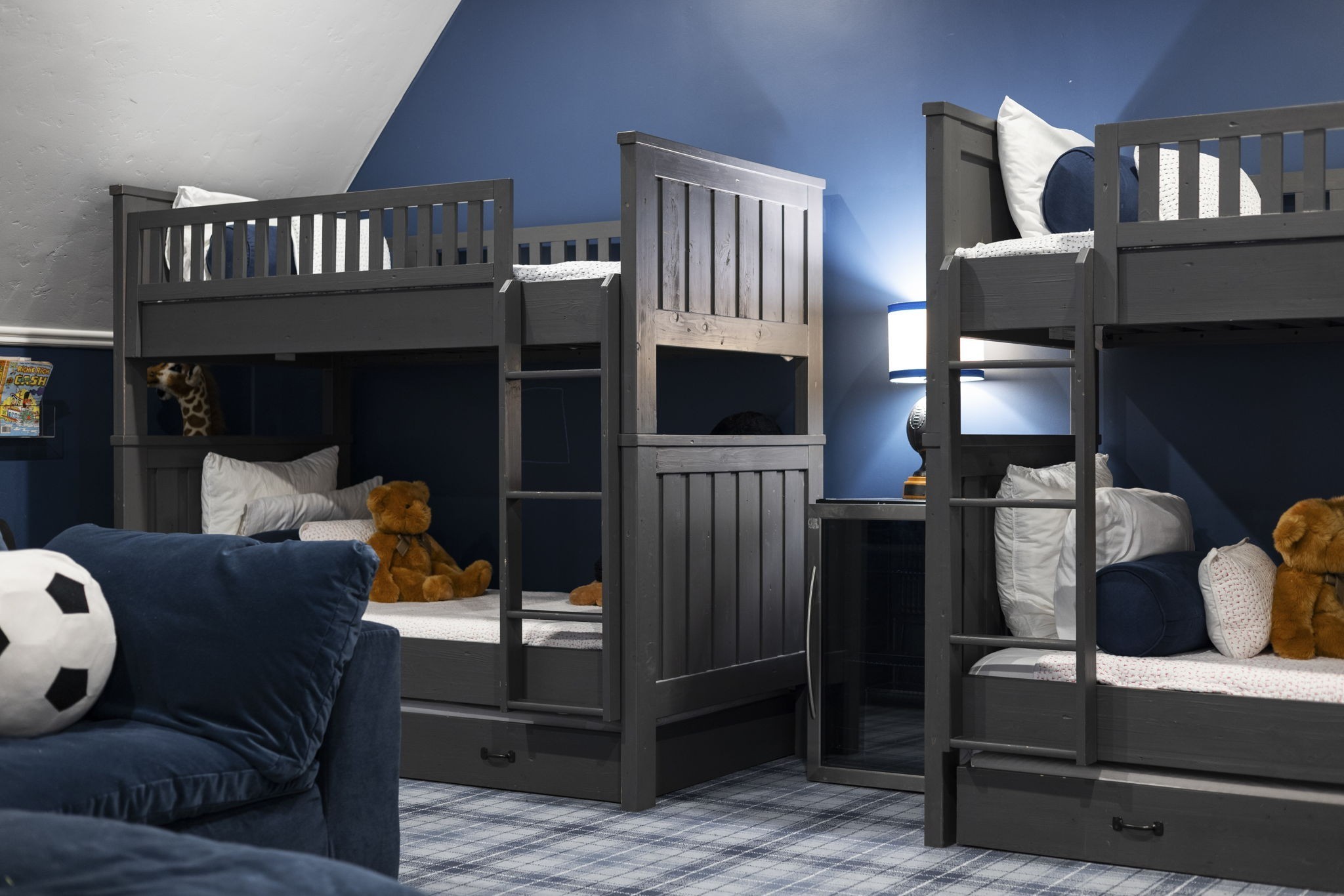 Bedroom with dark gray bunk beds, navy walls, a blue sofa, and stuffed animals.