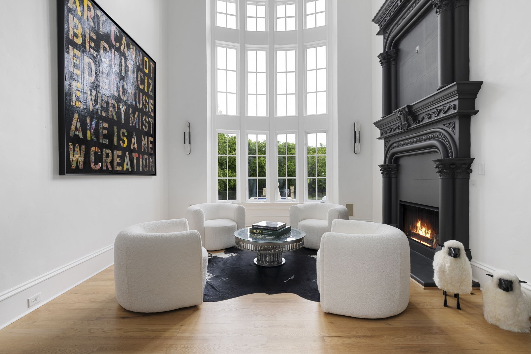 Living room with tall windows, white lounge chairs, and an ornate black fireplace.